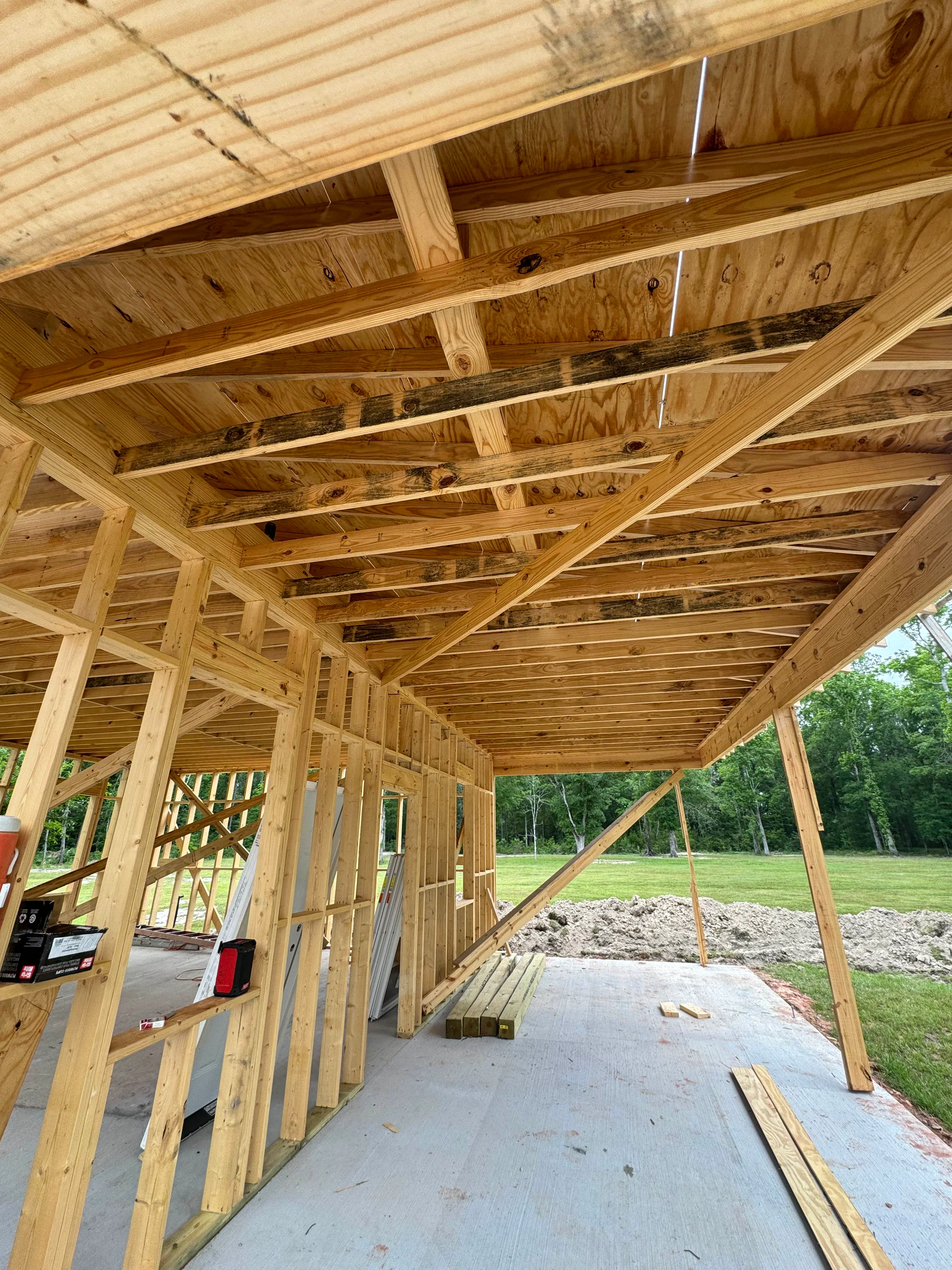 Interior view of residential wood framing with exposed beams, posts, and roof trusses under construction