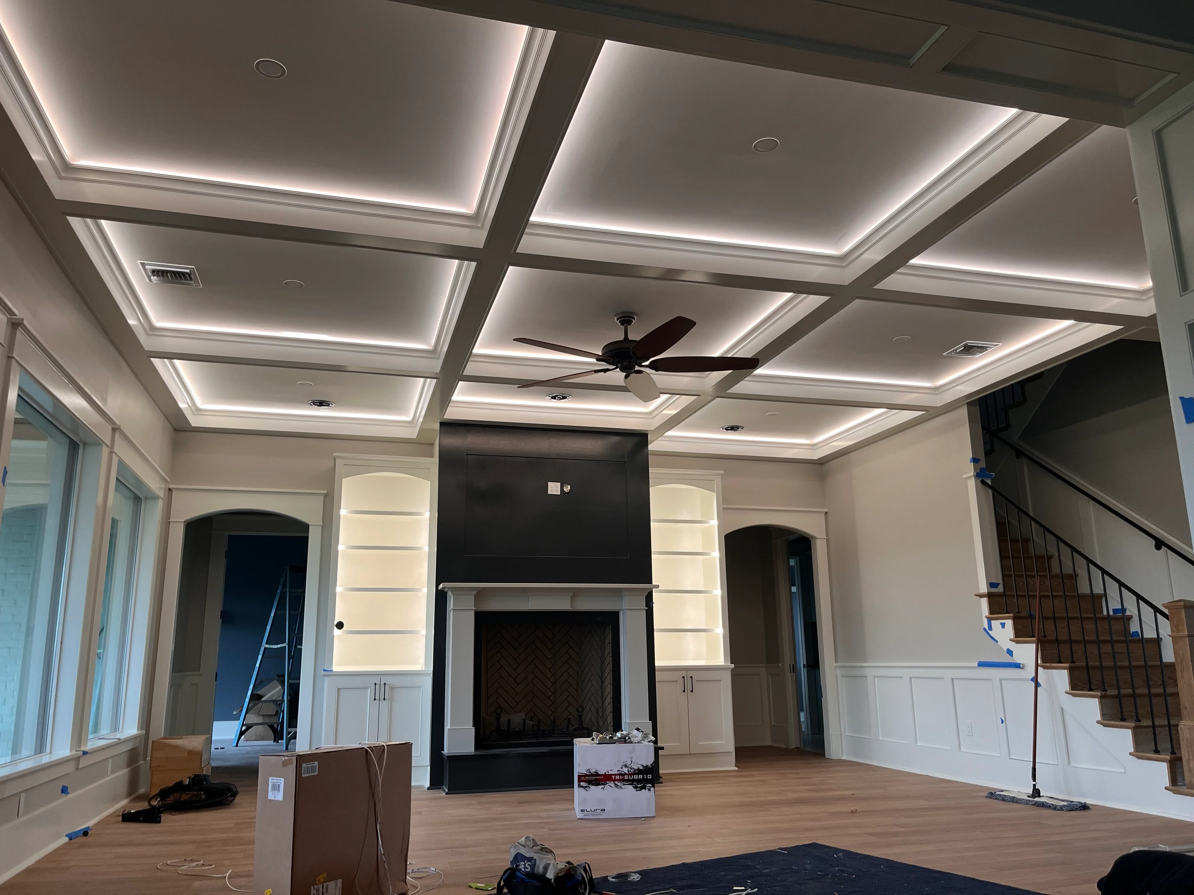 Modern great room with coffered ceiling, LED lighting, fireplace, and custom cabinetry