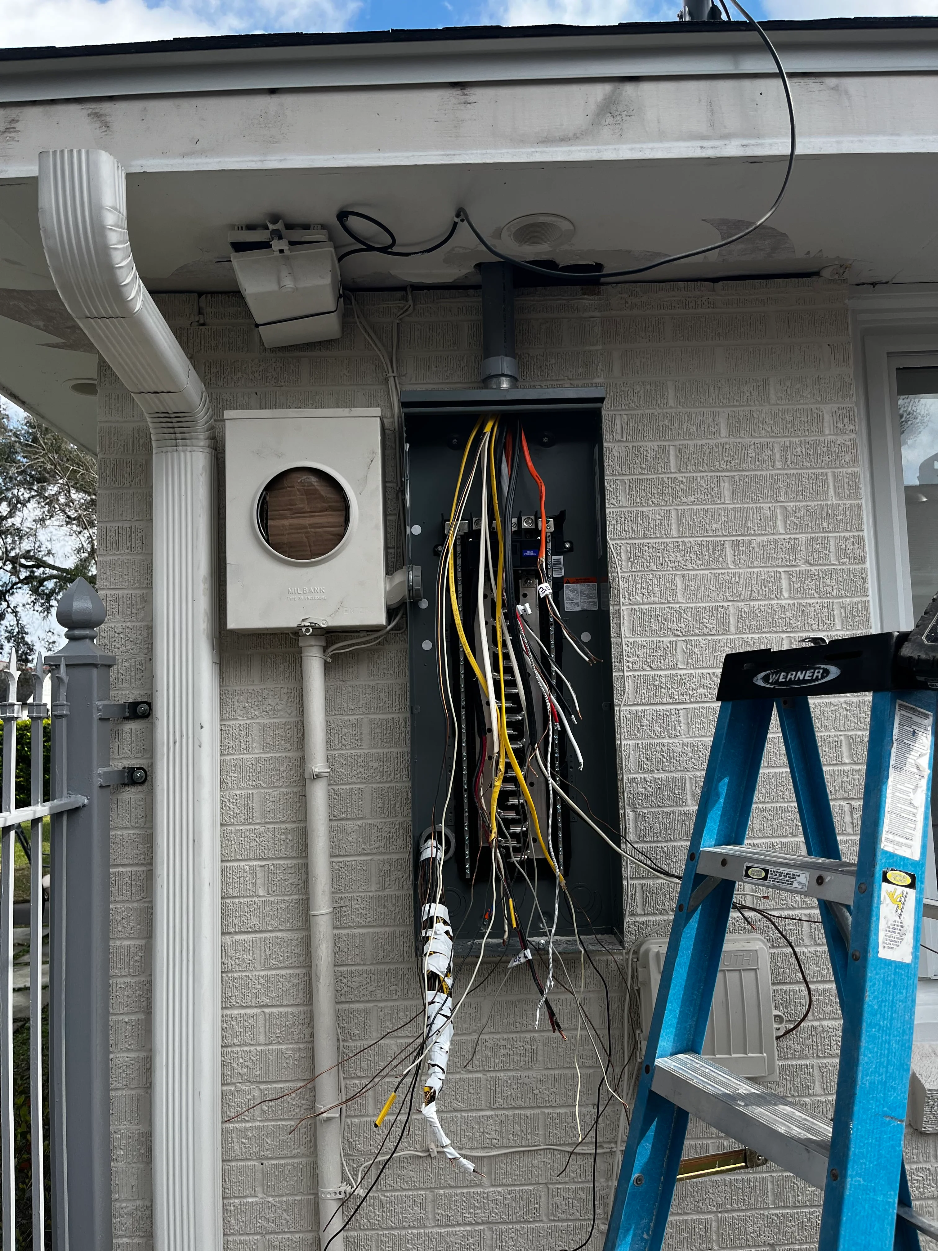 Electrical panel installation with organized wiring and white conduit on brick exterior