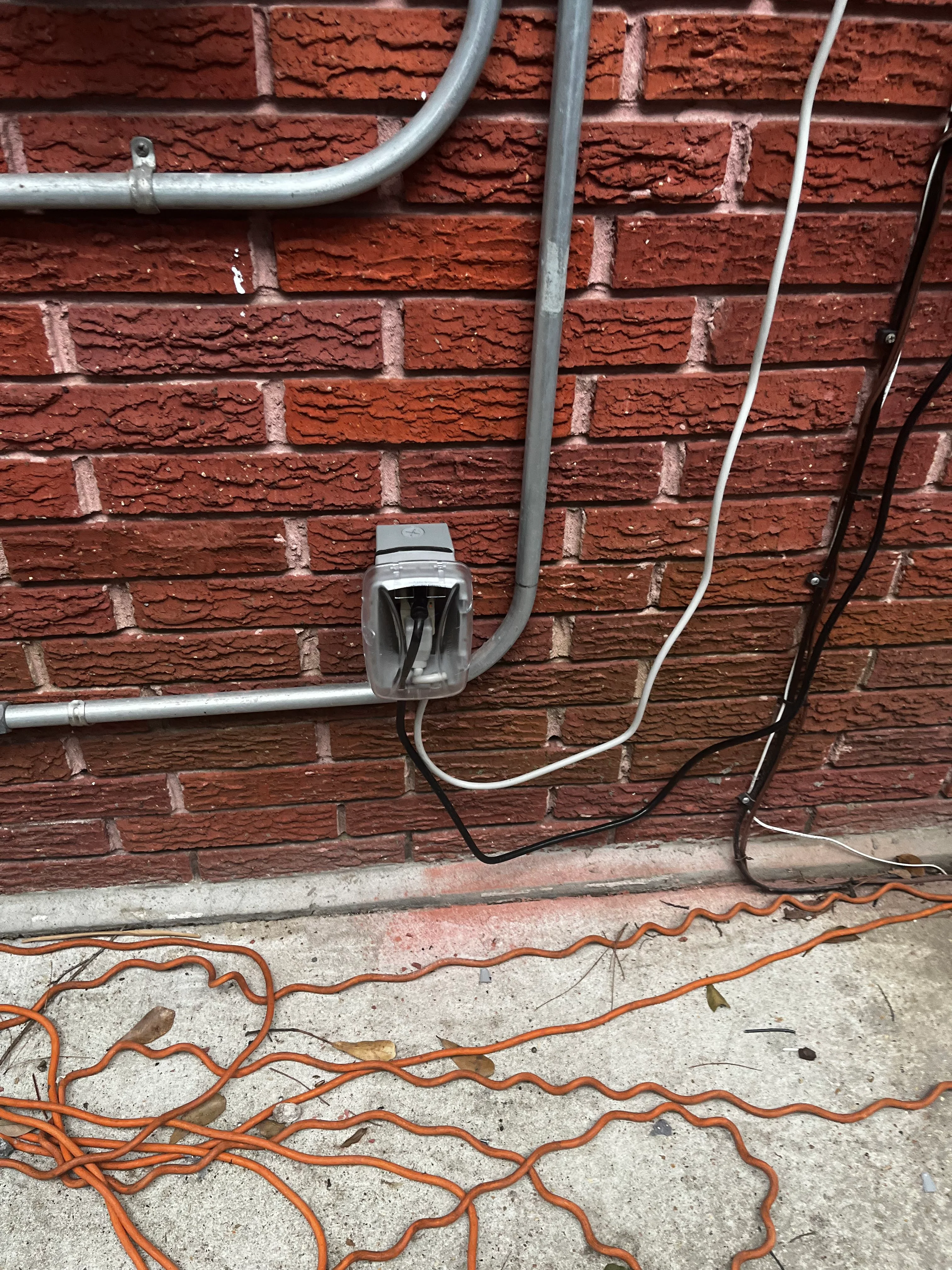 Exterior electrical conduit and weatherproof outlet installed on red brick wall