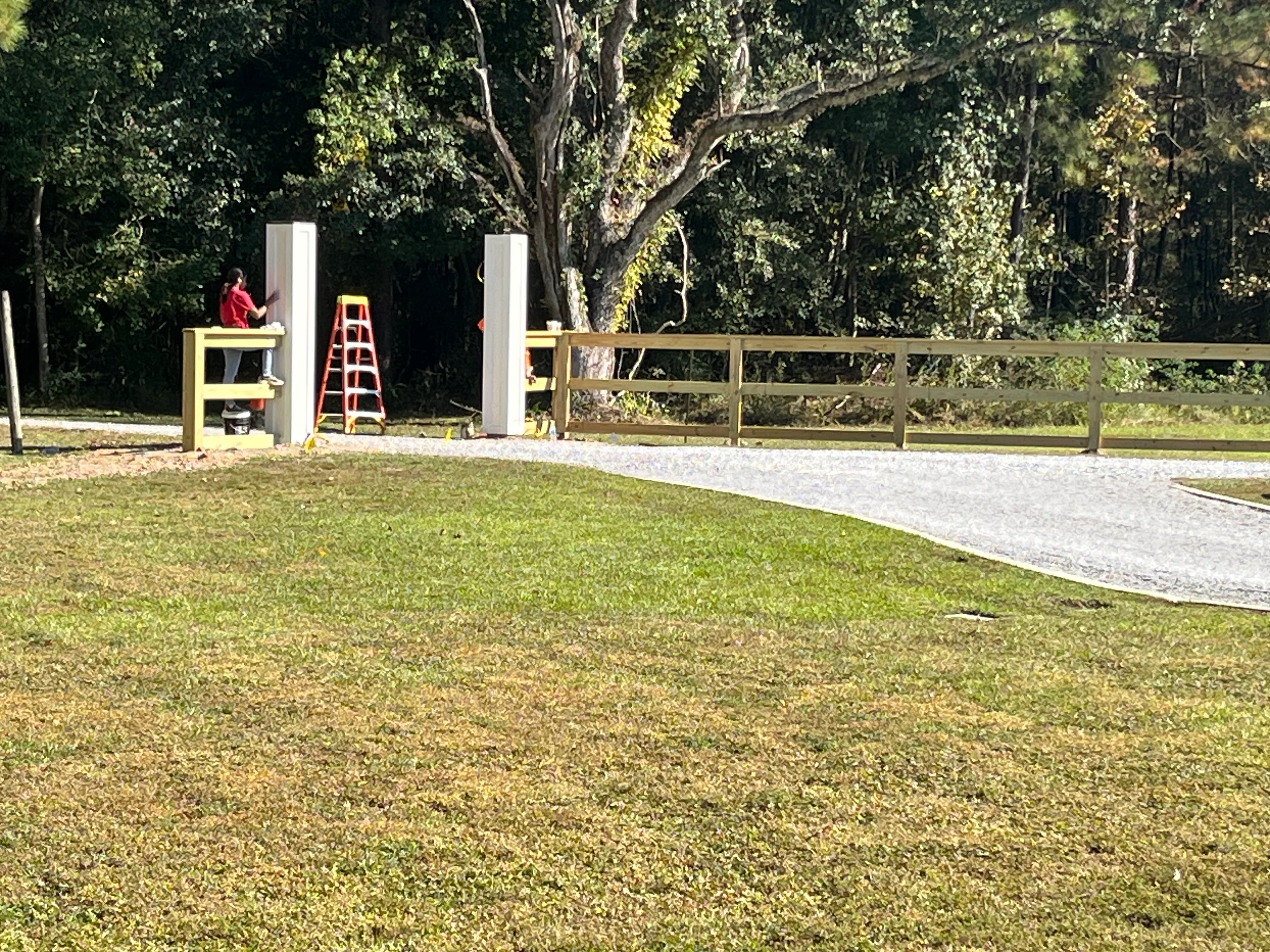 Newly installed concrete driveway with wooden rail fence and metal gate entrance on residential property