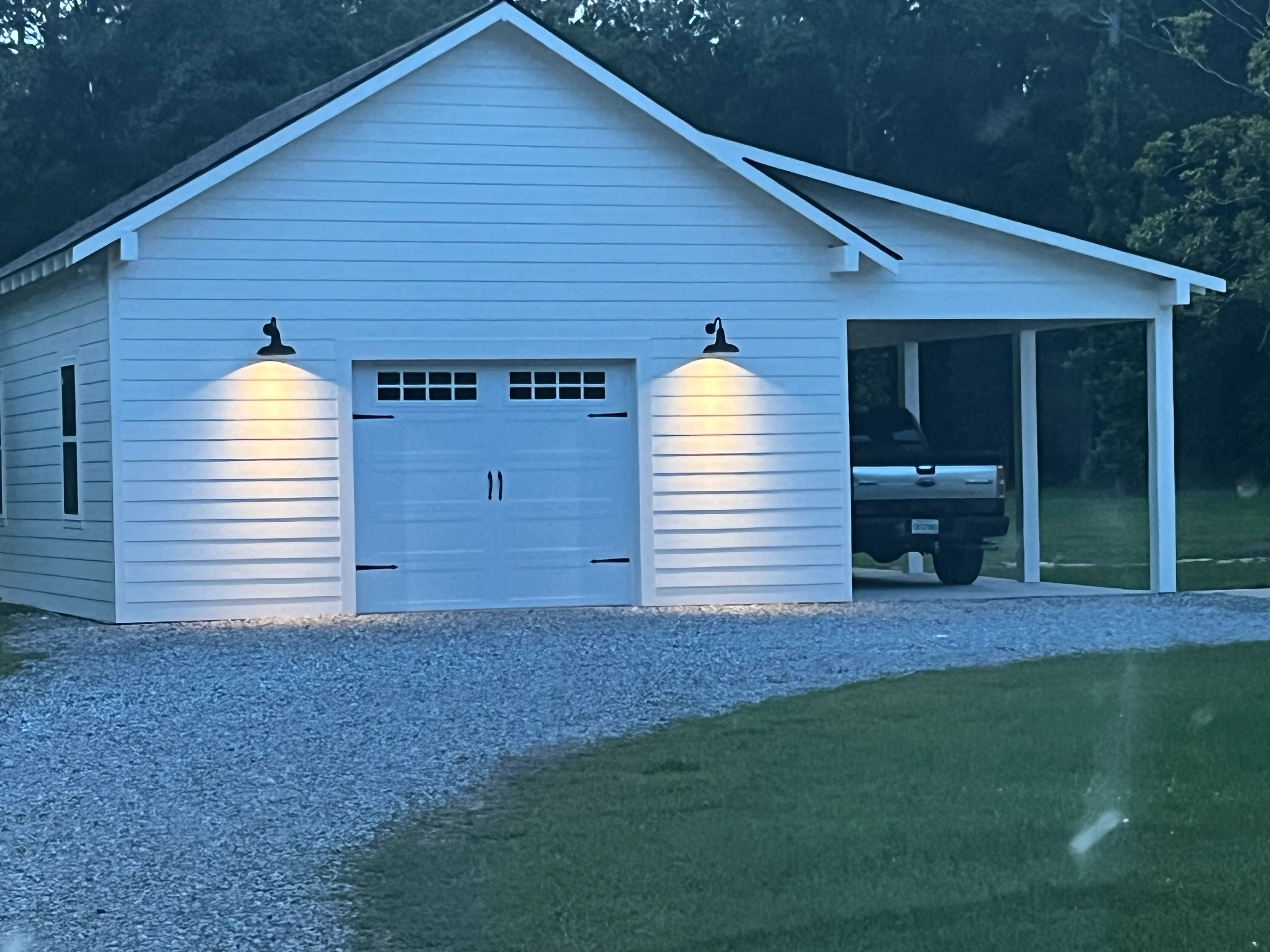 Modern light blue garage with two-car doors and covered carport at dusk with landscape lighting