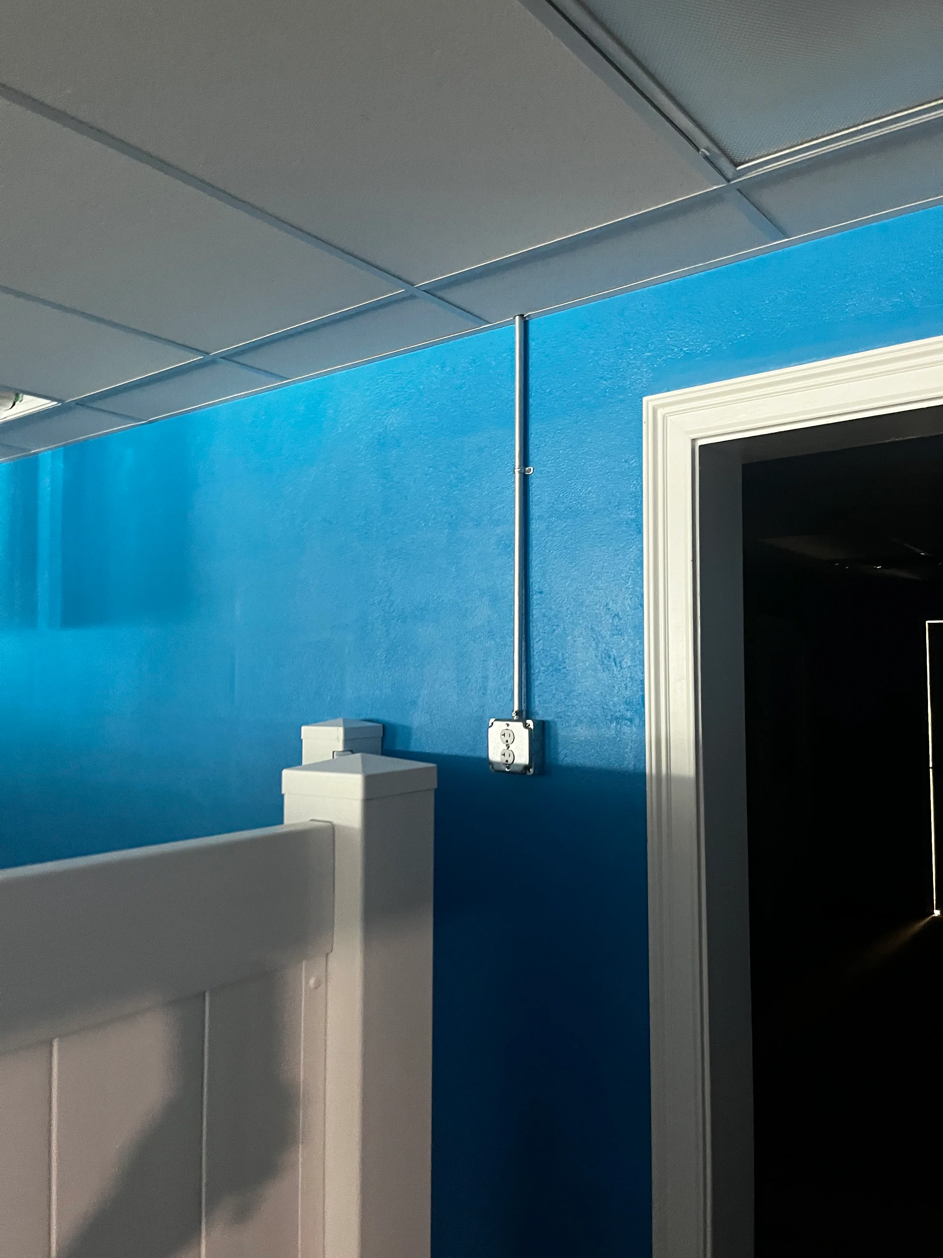 Blue painted drywall with white trim, suspended ceiling, and electrical outlet installation