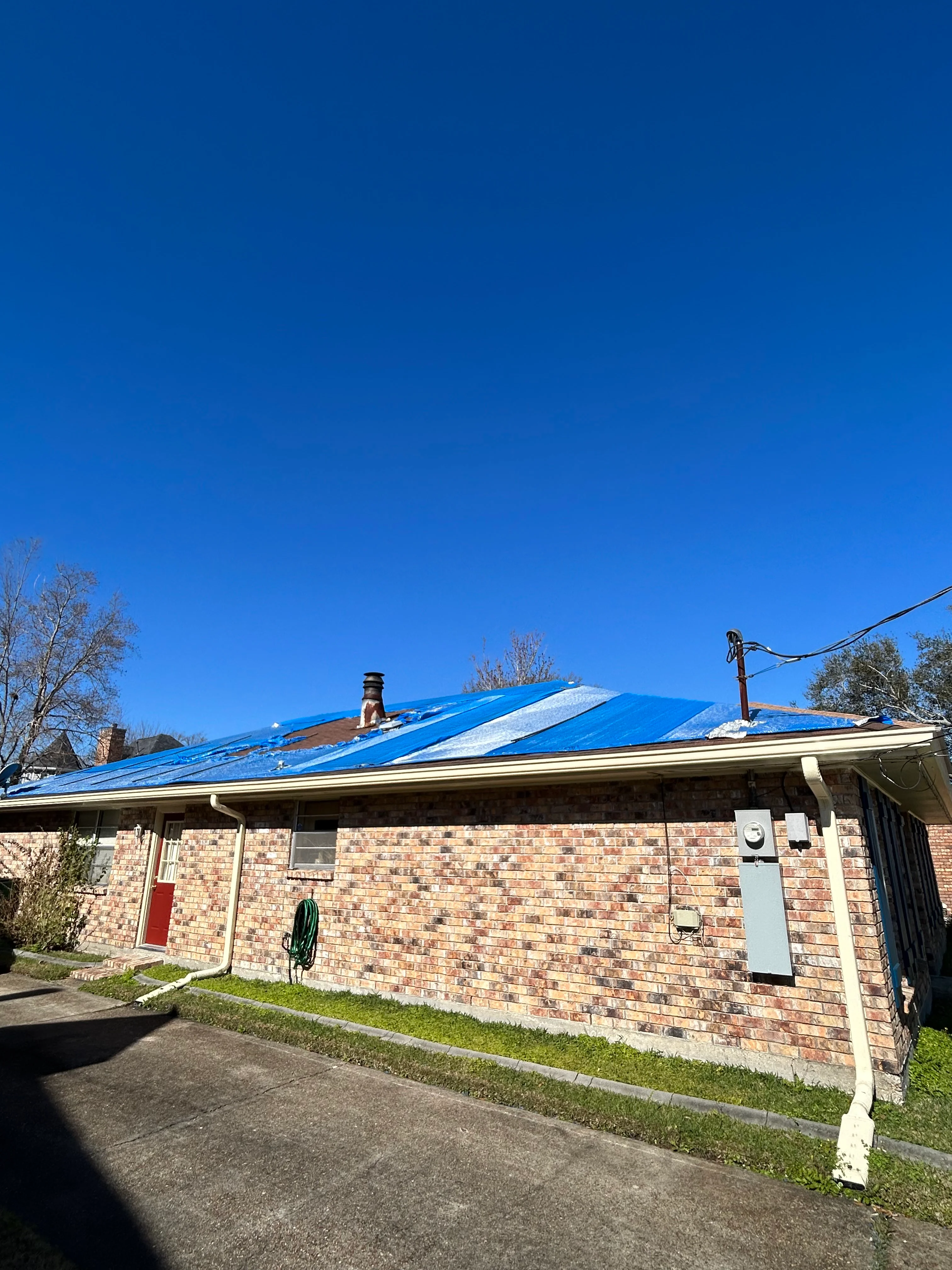 Brick home with newly installed blue metal roof against clear sky
