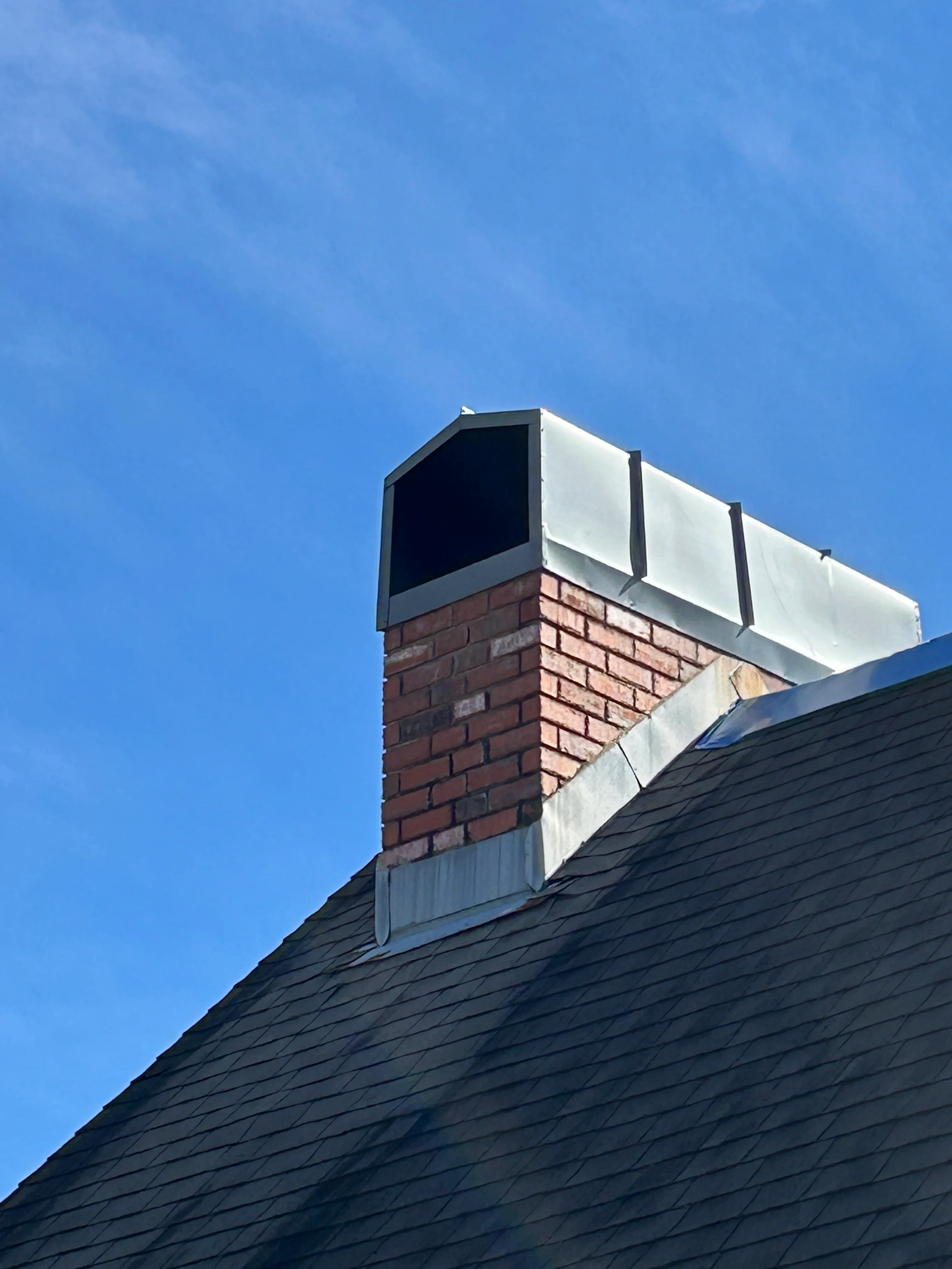 Brick chimney with metal flashing and cap installed on dark asphalt shingle roof