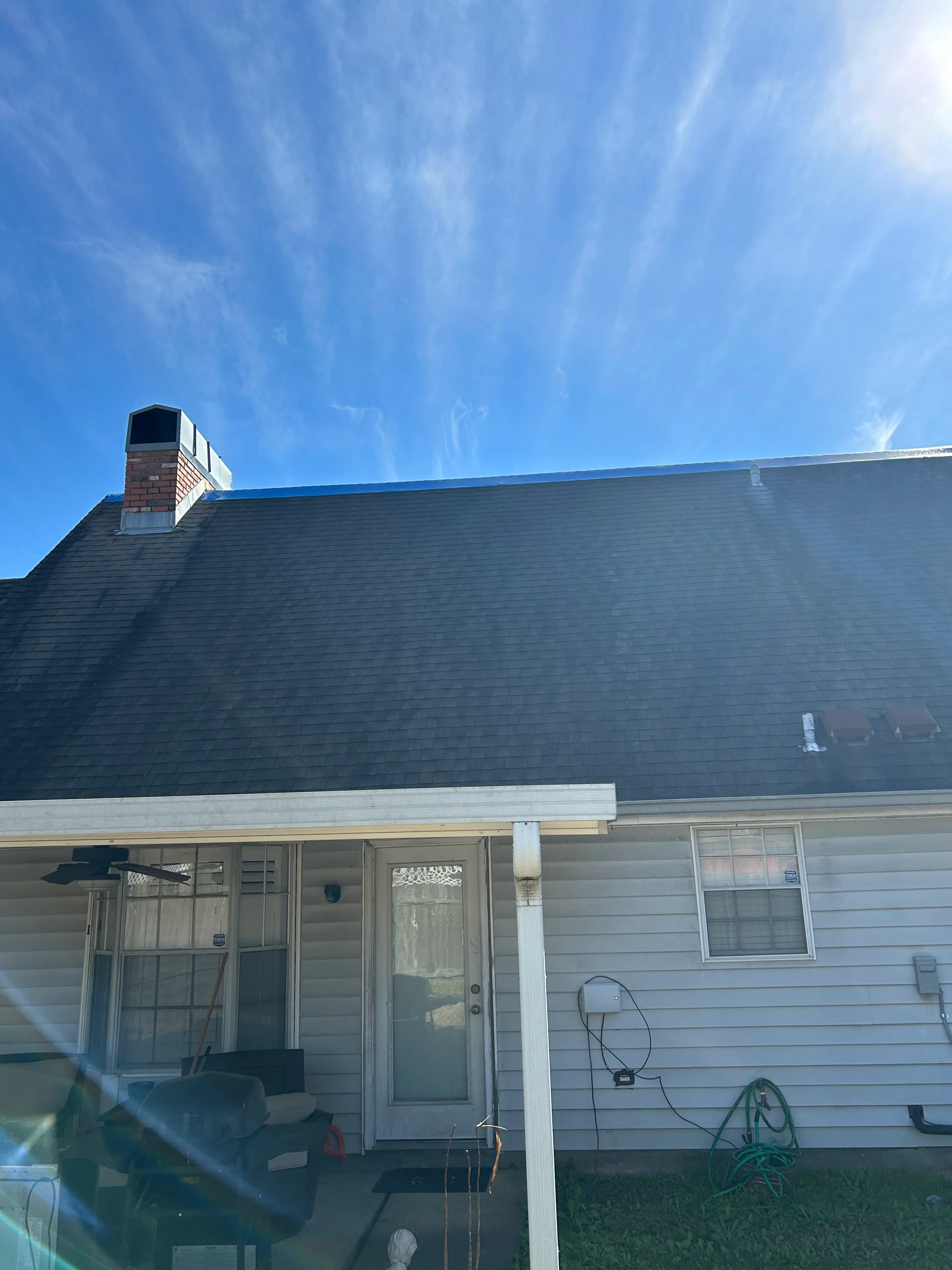 Residential home with newly installed slate gray architectural shingles and brick chimney against clear blue sky