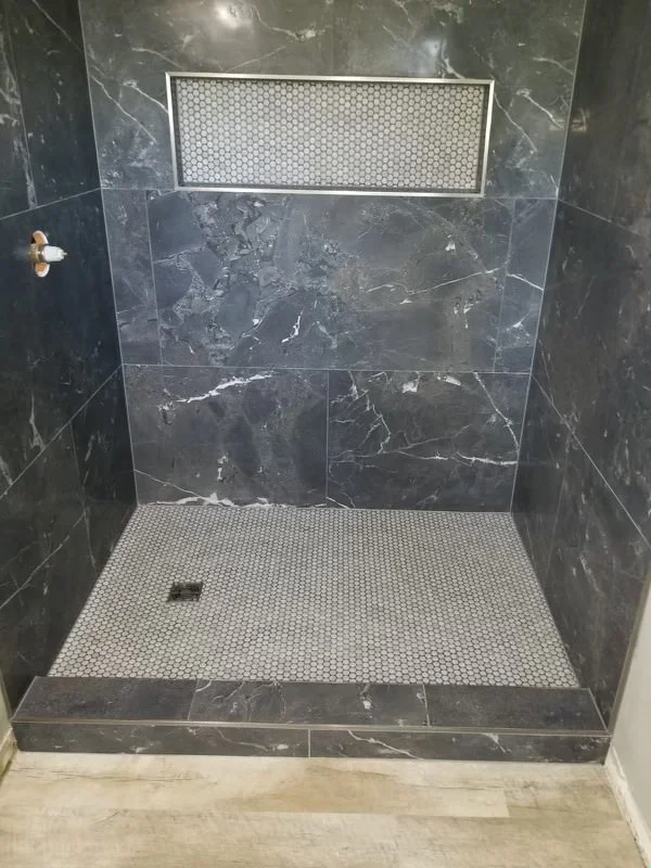 Dark marble shower with white penny-round tile floor and matching niche