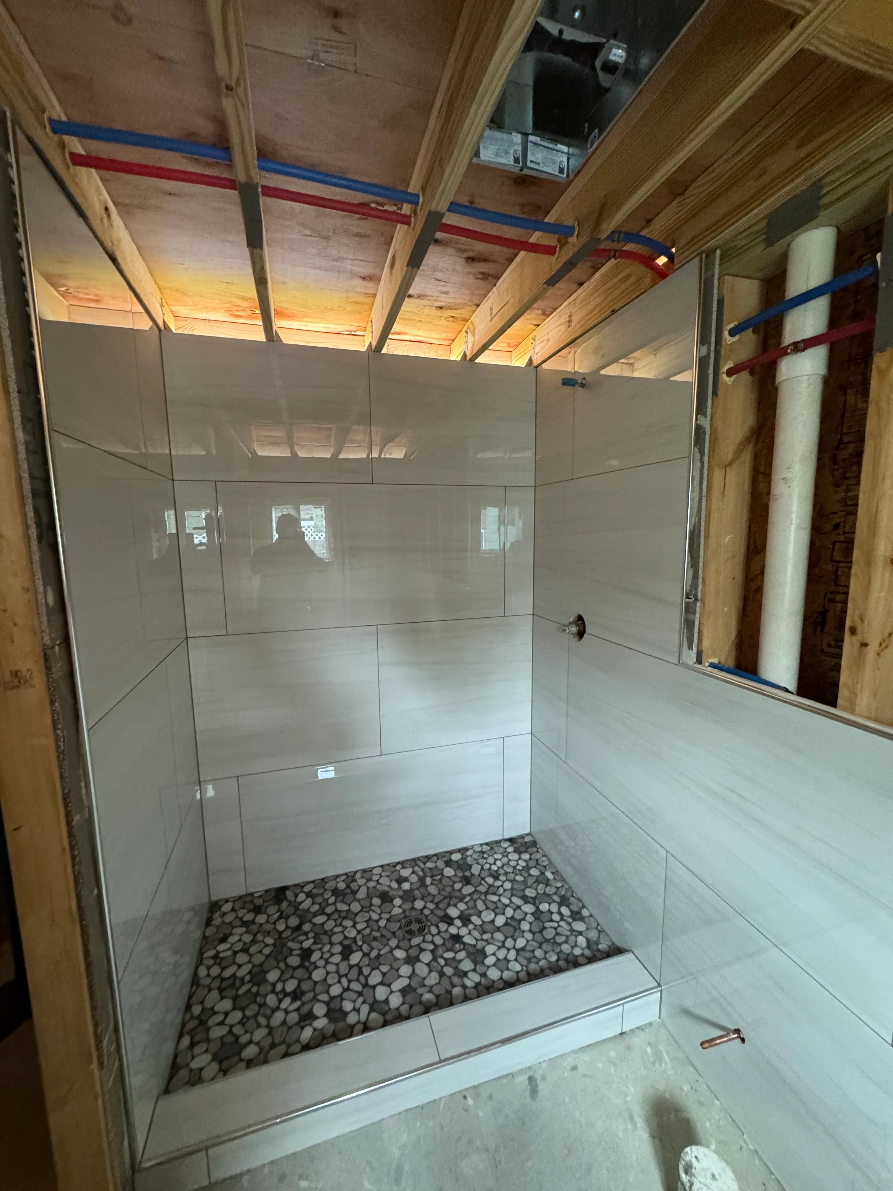 Newly tiled shower enclosure with glass door and river rock floor in construction phase