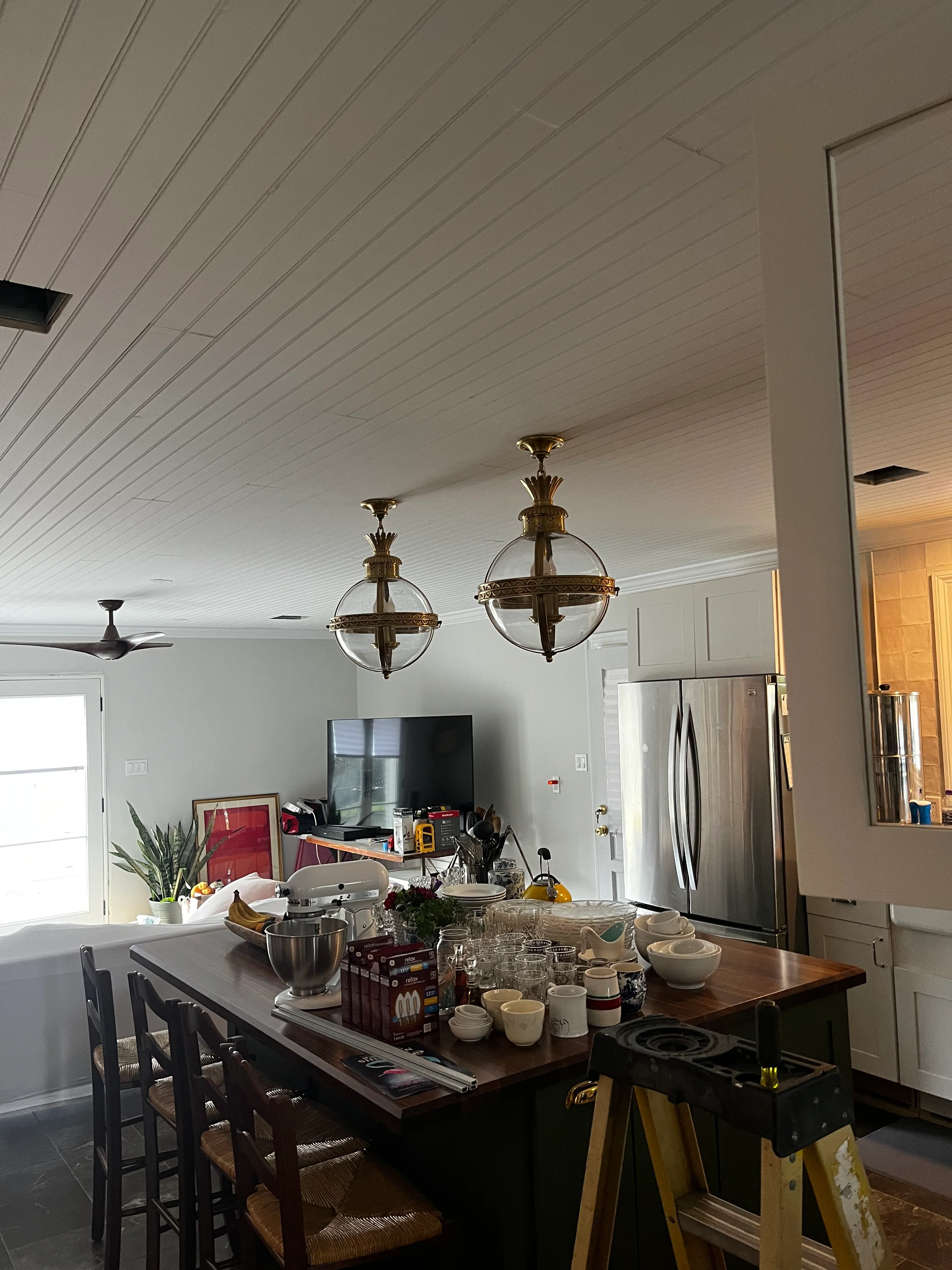 Modern kitchen with white shiplap ceiling, brass pendant lights, dark wood island, and stainless steel appliances