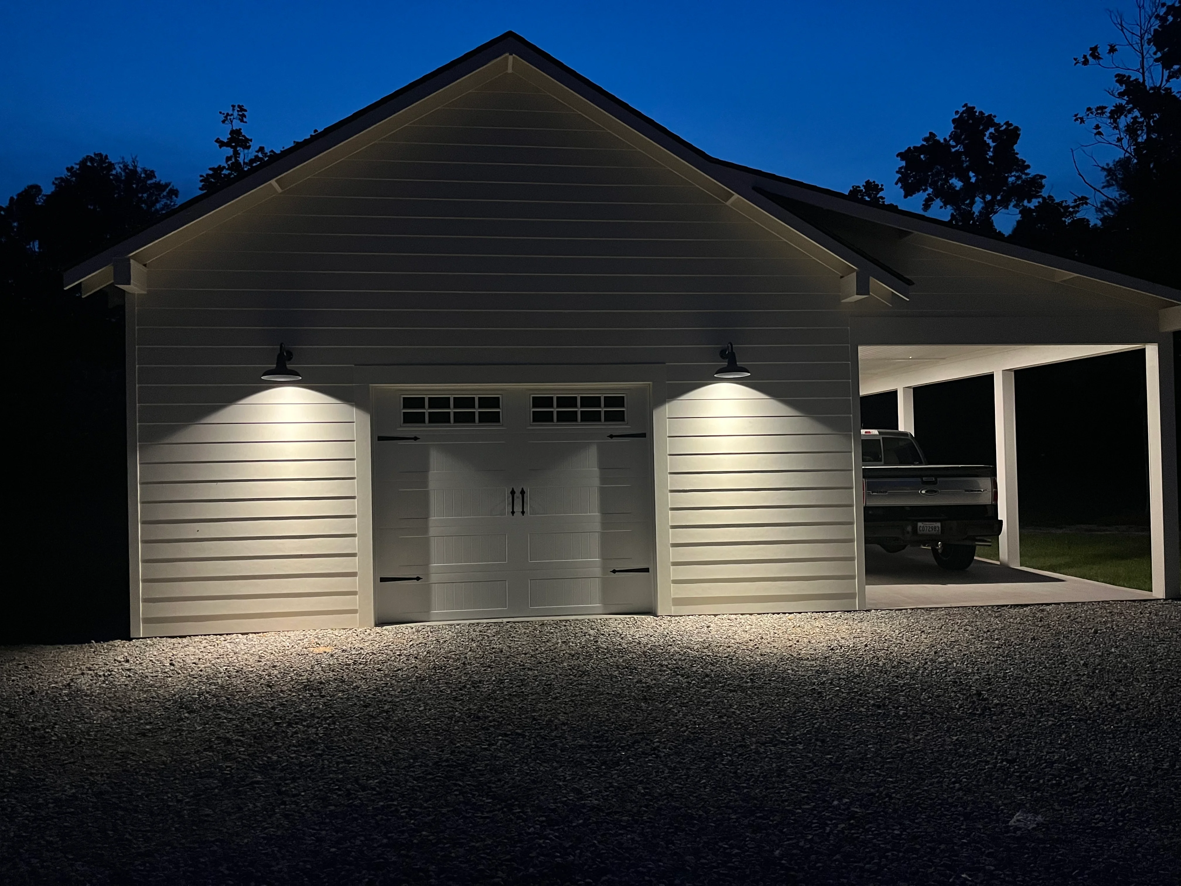 Modern gray garage with carport addition, lit by overhead fixtures at dusk
