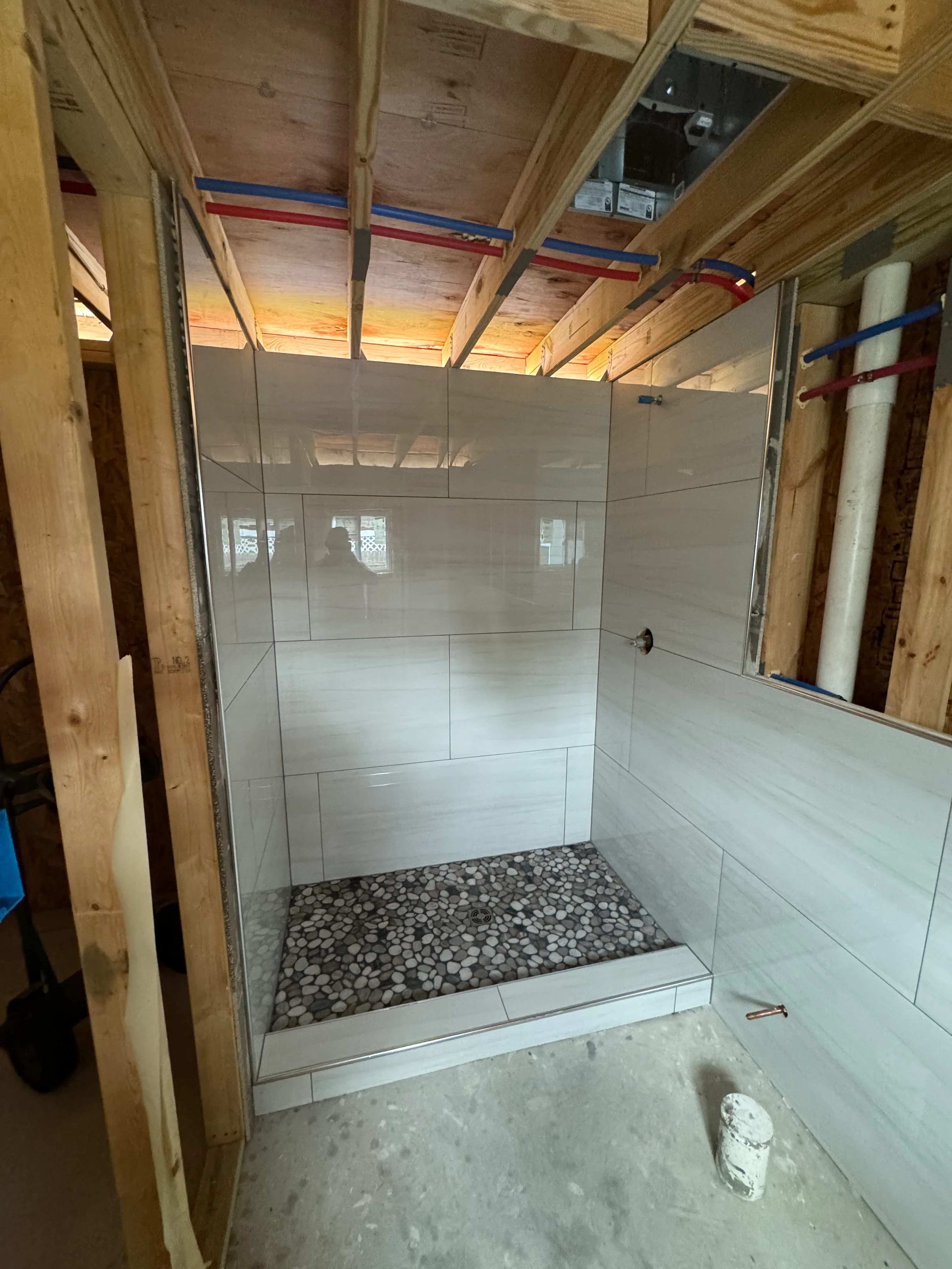 Walk-in shower with white subway tiles, pebble floor, and frameless glass doors under construction