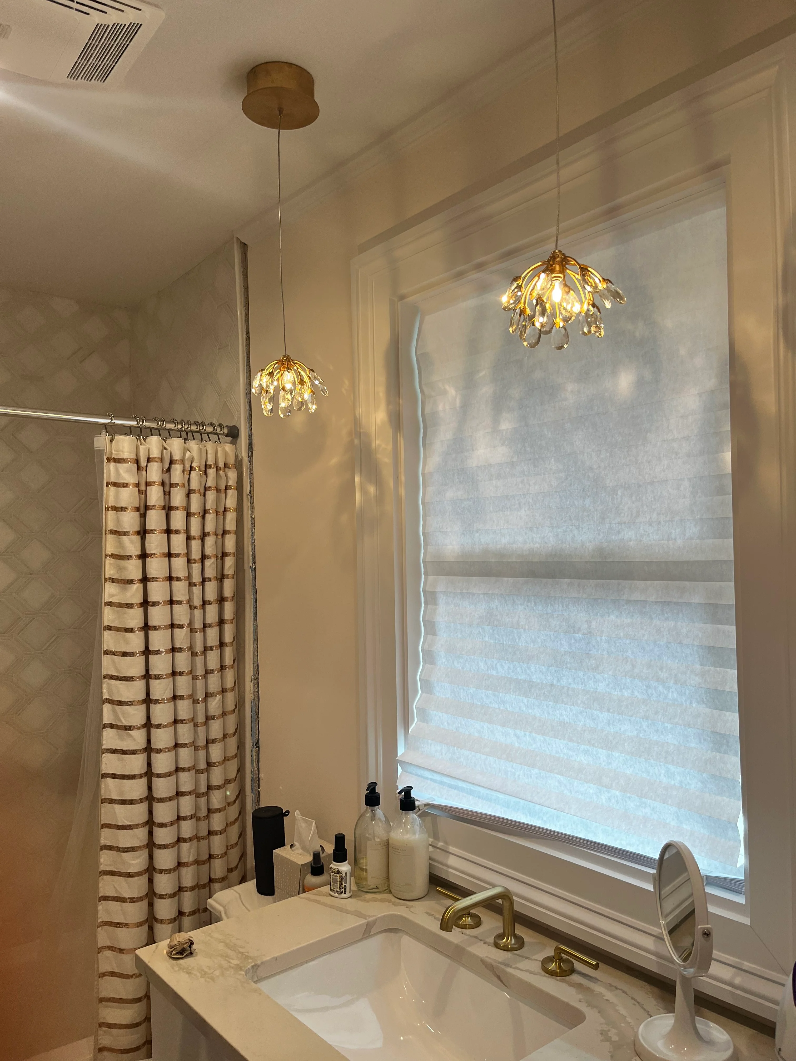 Renovated bathroom with brass pendant lights, marble vanity, and cellular window shades