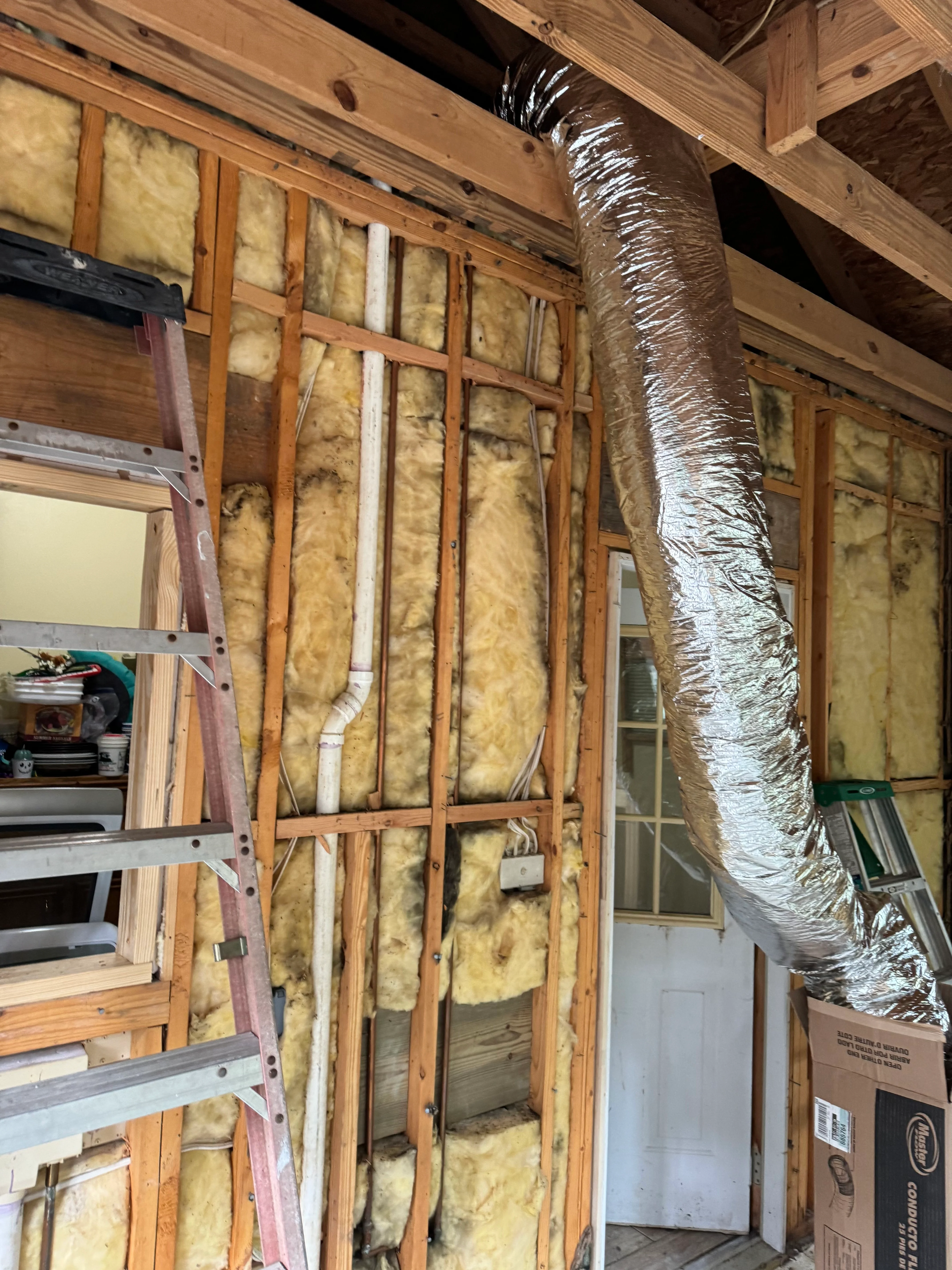Wooden stud framing with yellow fiberglass insulation and wrapped HVAC ductwork during interior construction