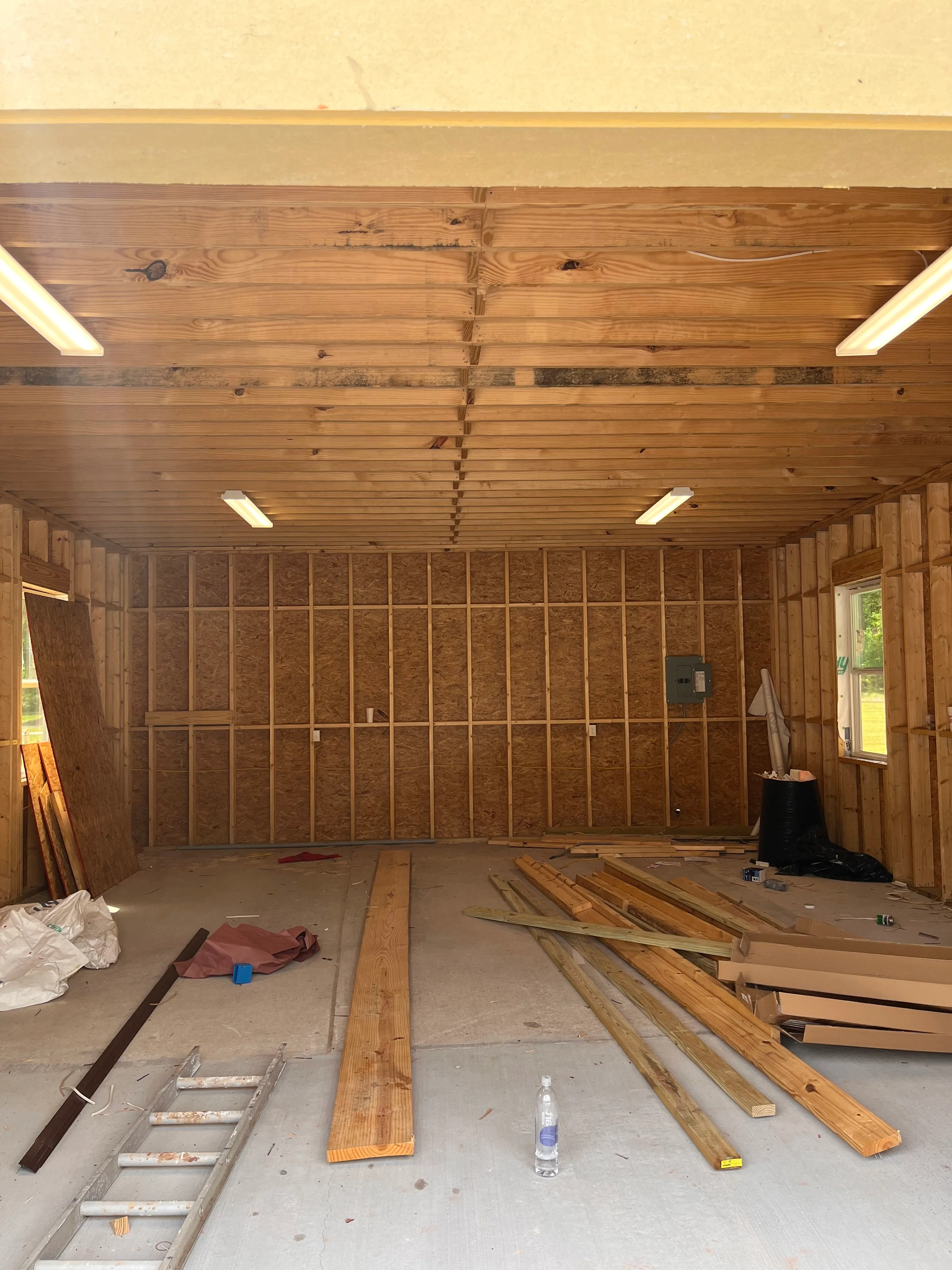 Interior framing with insulation batts, wooden ceiling joists, and recessed lighting in residential garage