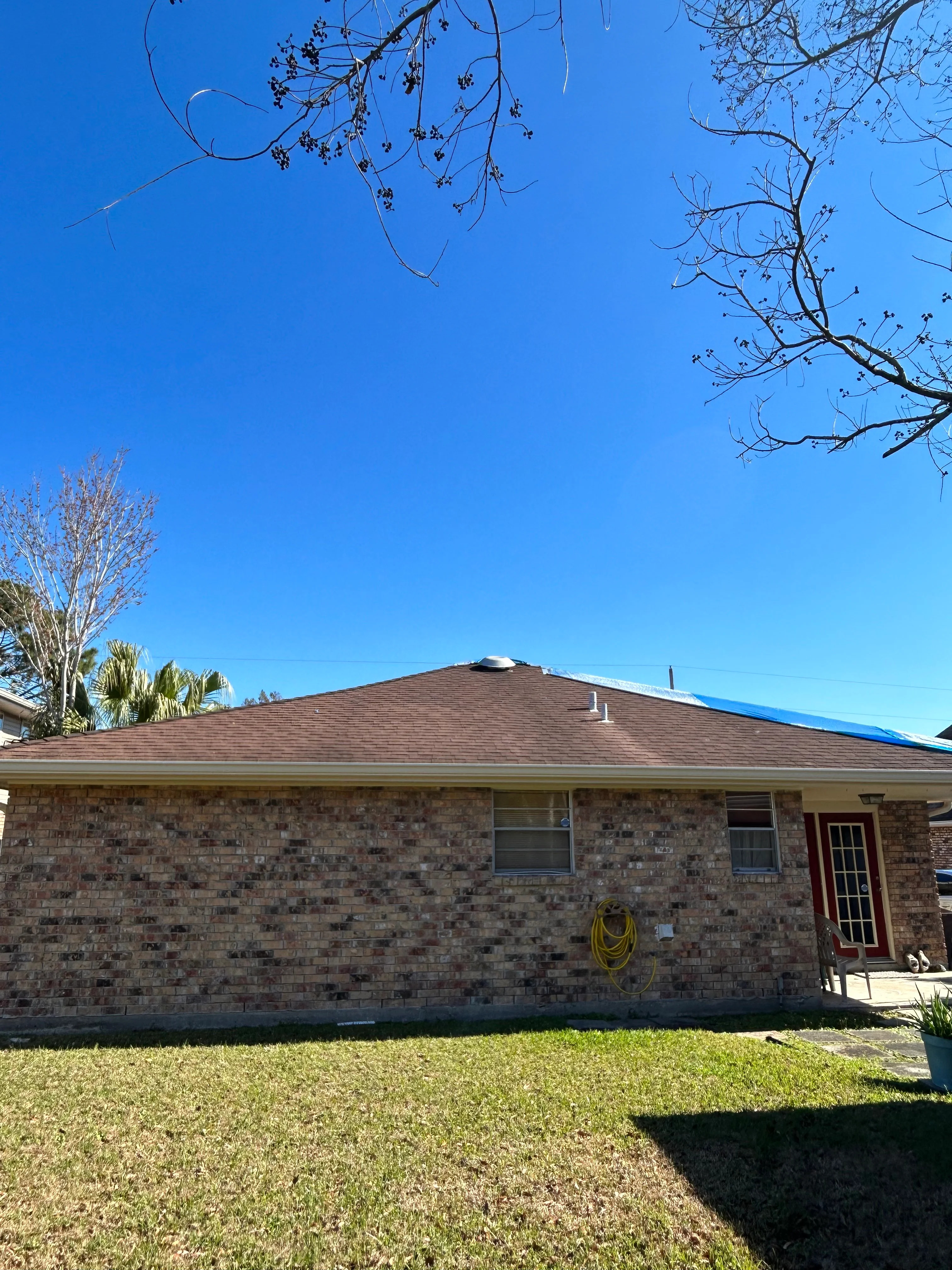 New brown architectural shingle roof on single-story brick home with clear blue sky