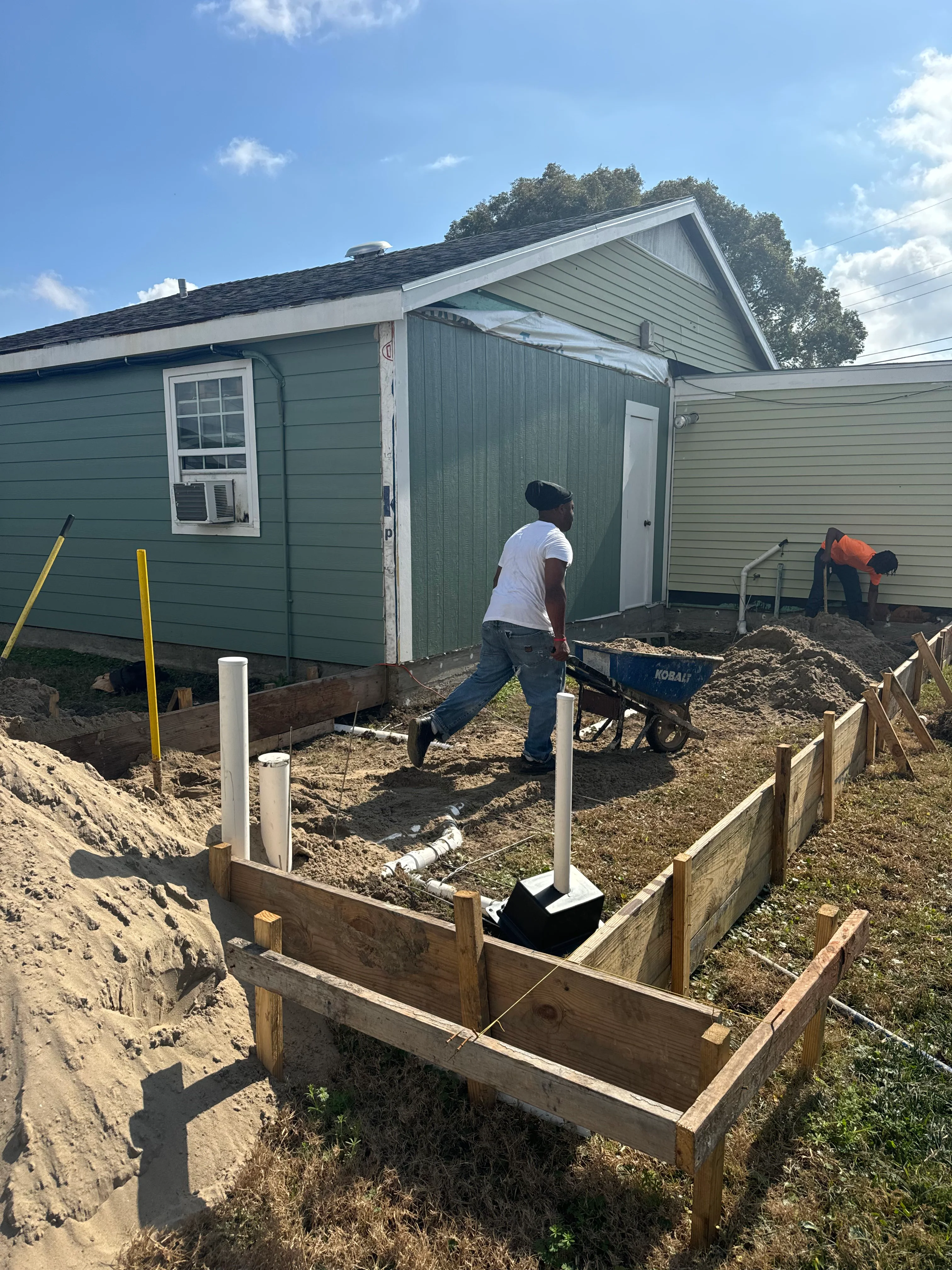 Construction crew preparing foundation with wooden framing and graded soil on residential site