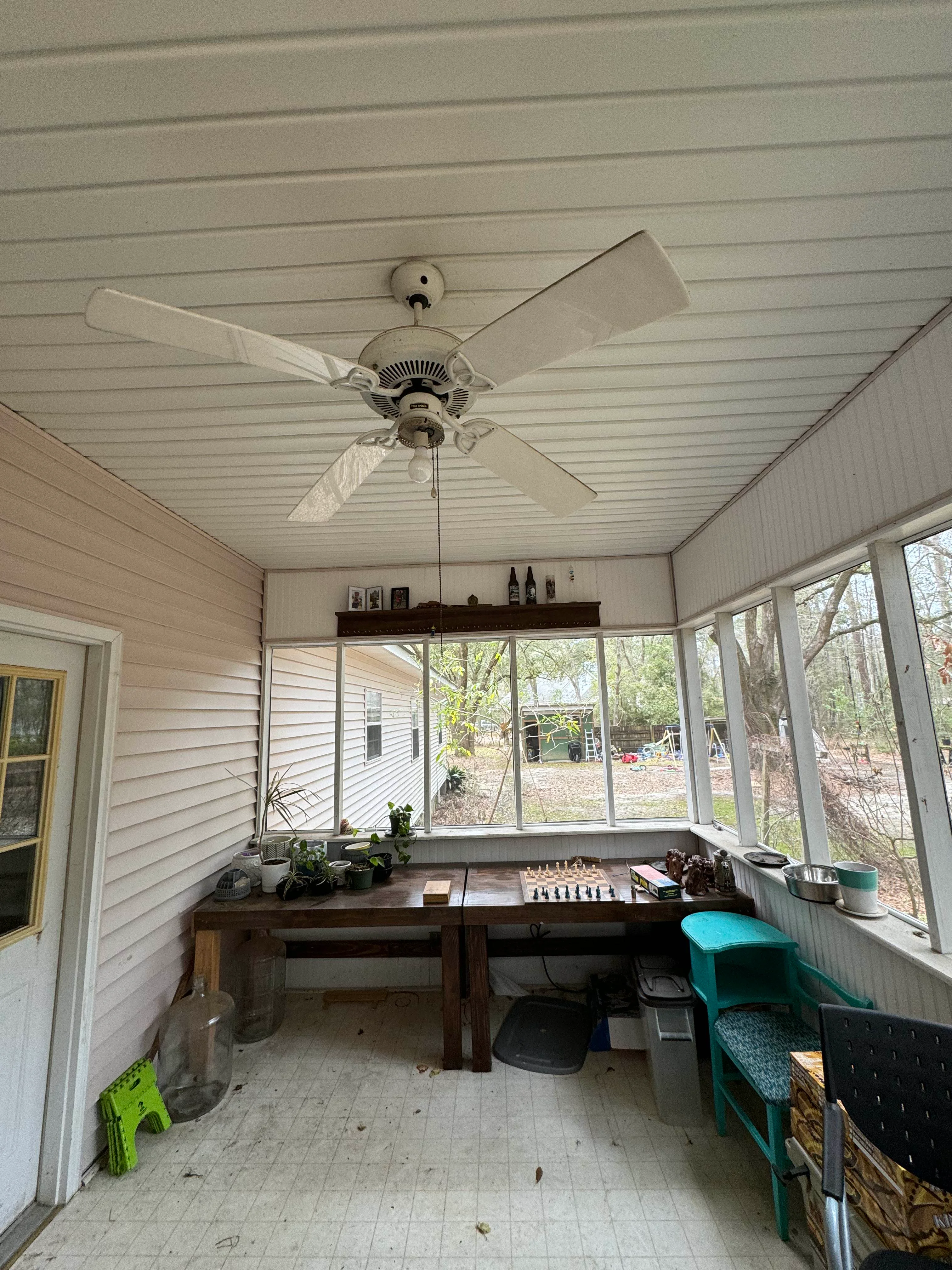 Bright screened porch with white siding, metal ceiling, ceiling fan, and large windows overlooking yard