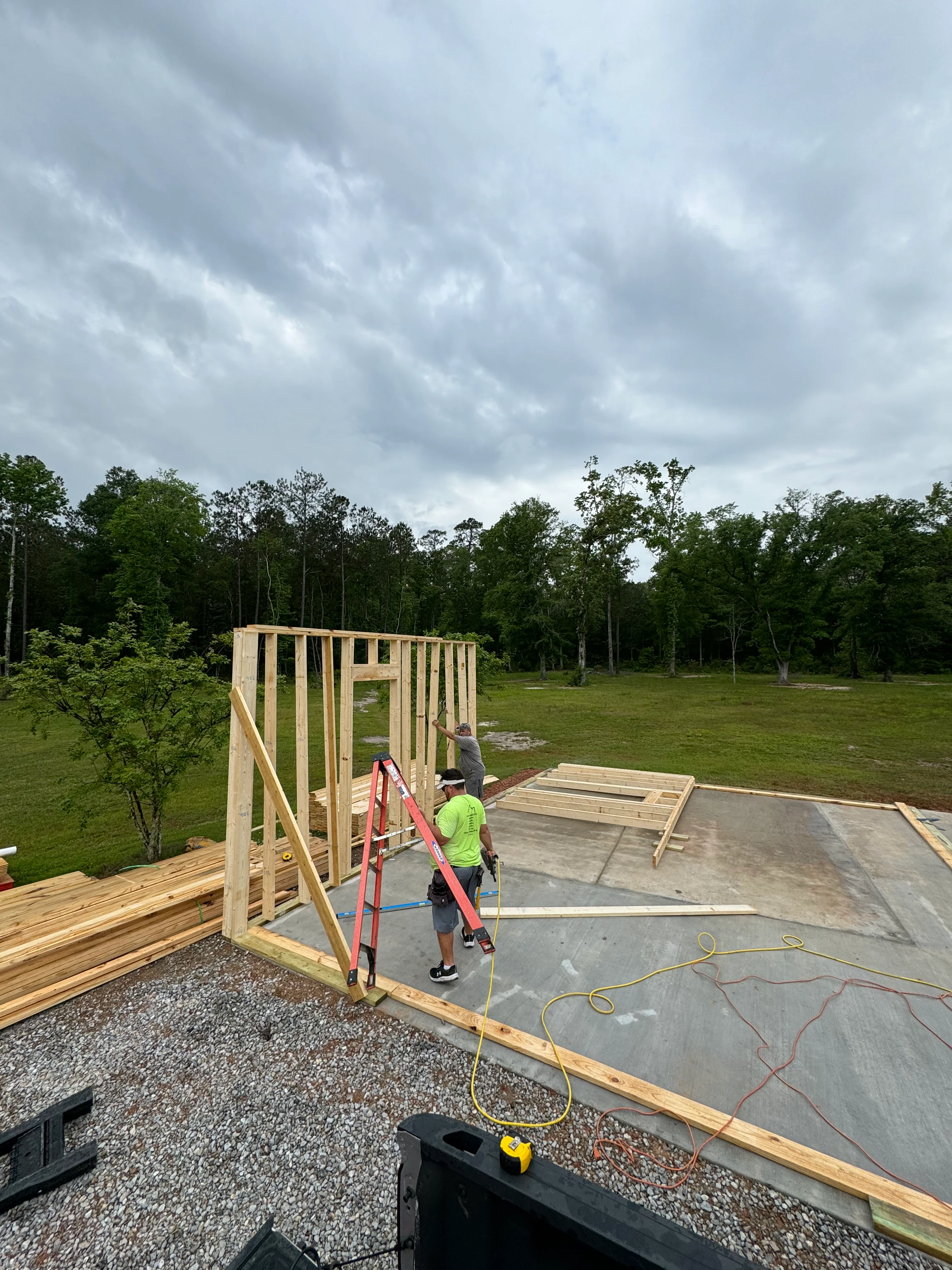Construction crew framing wooden walls on concrete foundation with forested lot in background