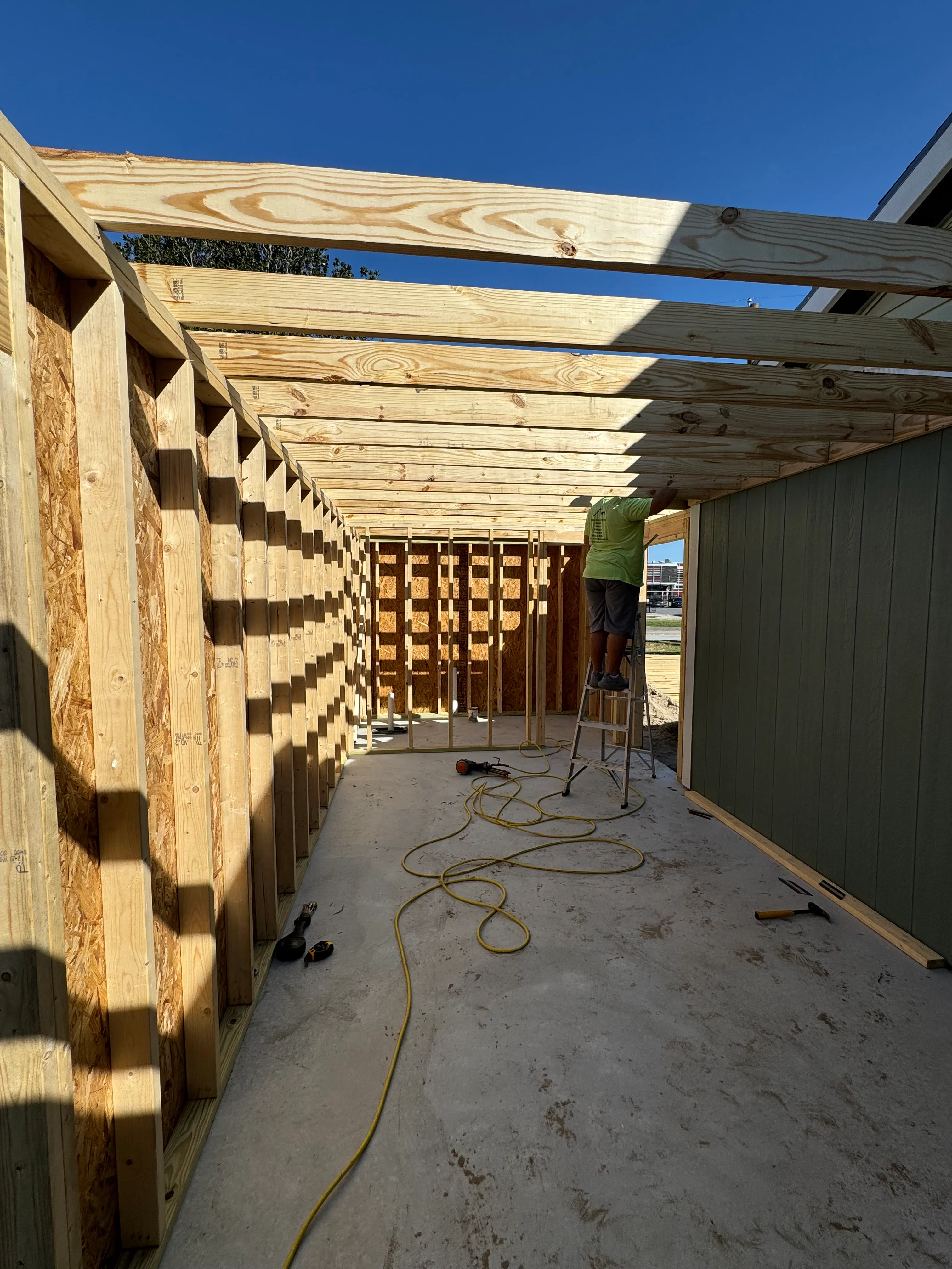 Wooden framing and pergola structure under construction with concrete foundation and tools on site