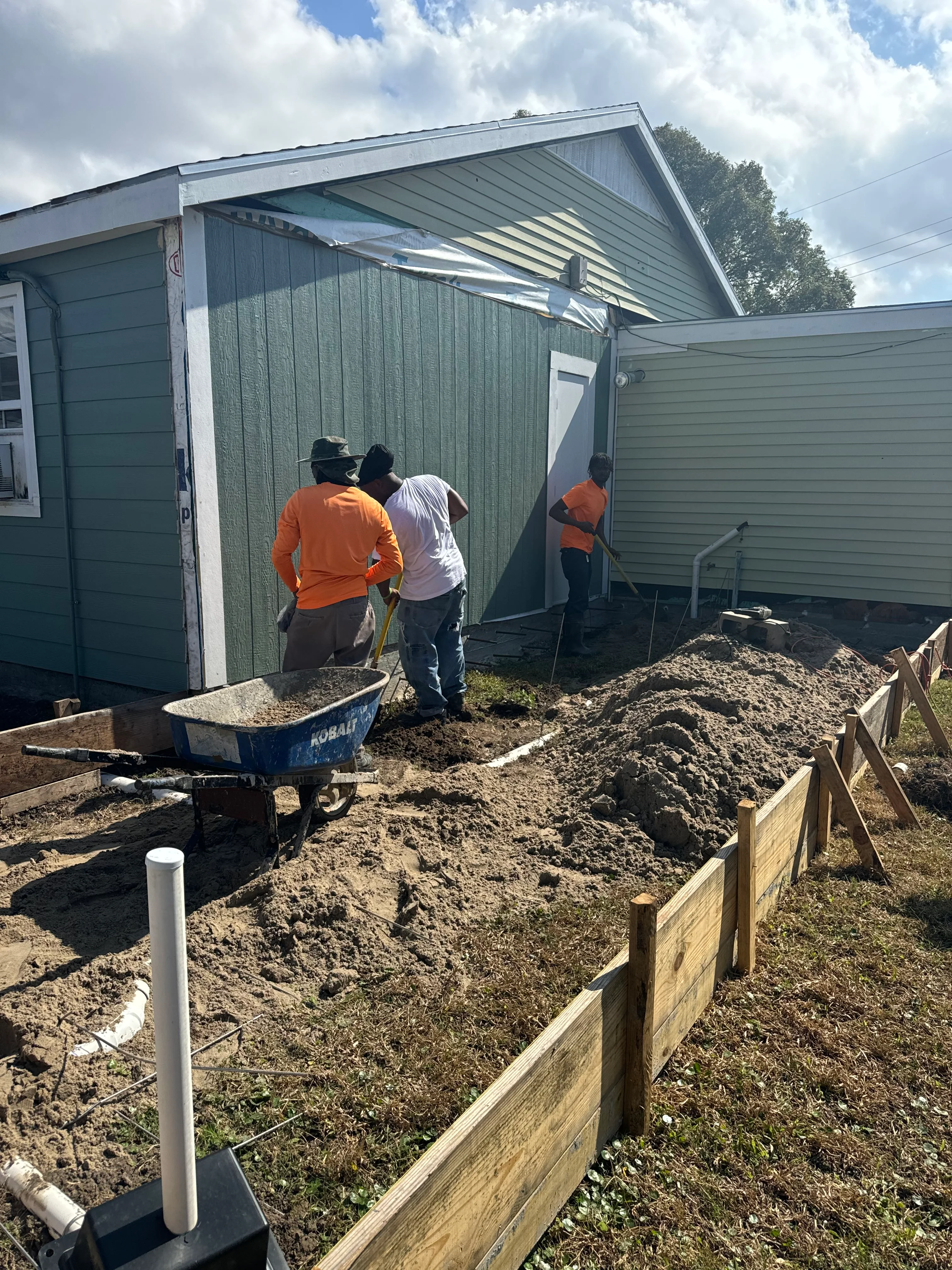 Construction crew grading residential site with metal storage structures and wooden retaining walls