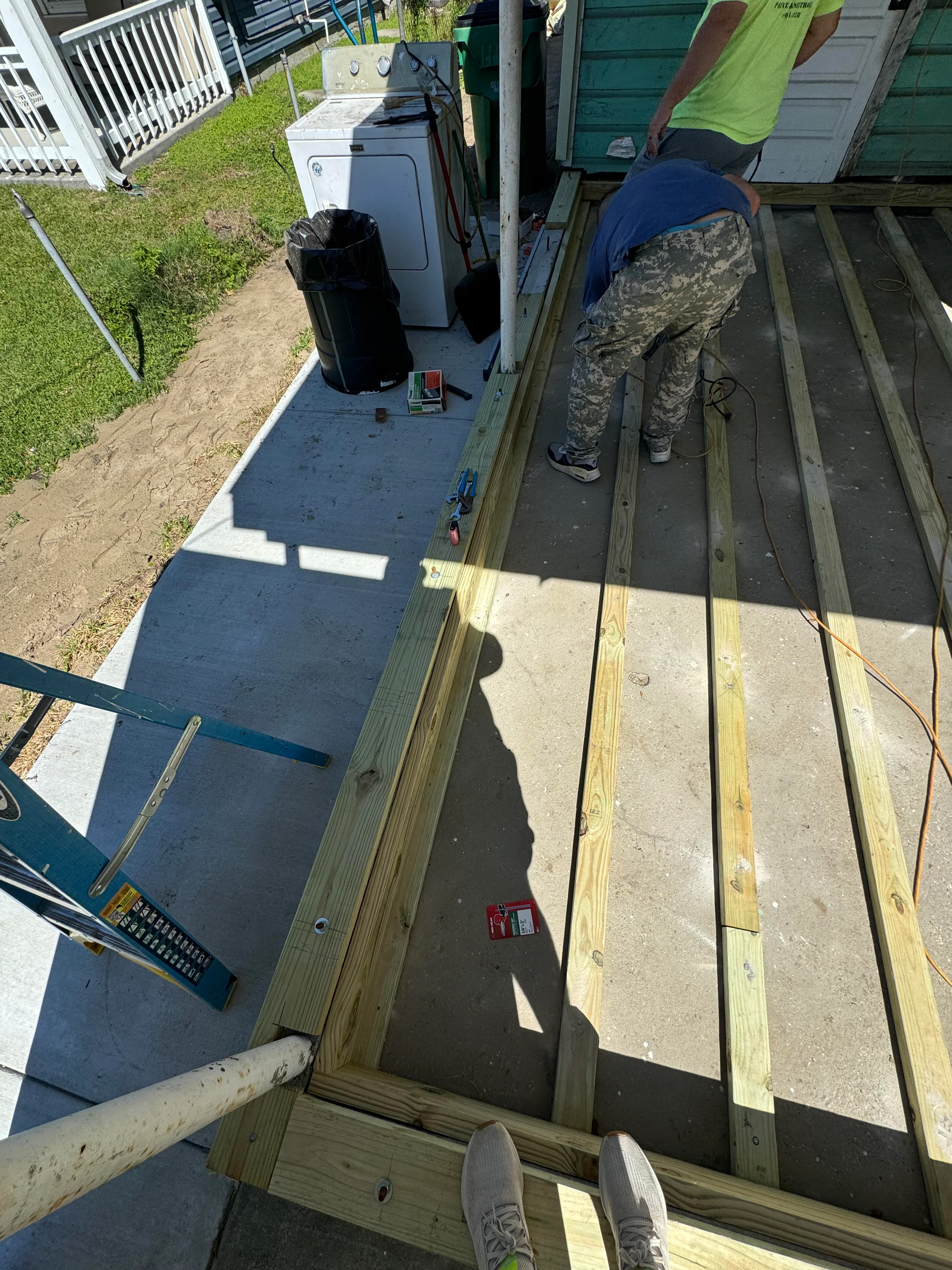Worker installing composite deck boards over pressure-treated lumber framing with utility pad visible