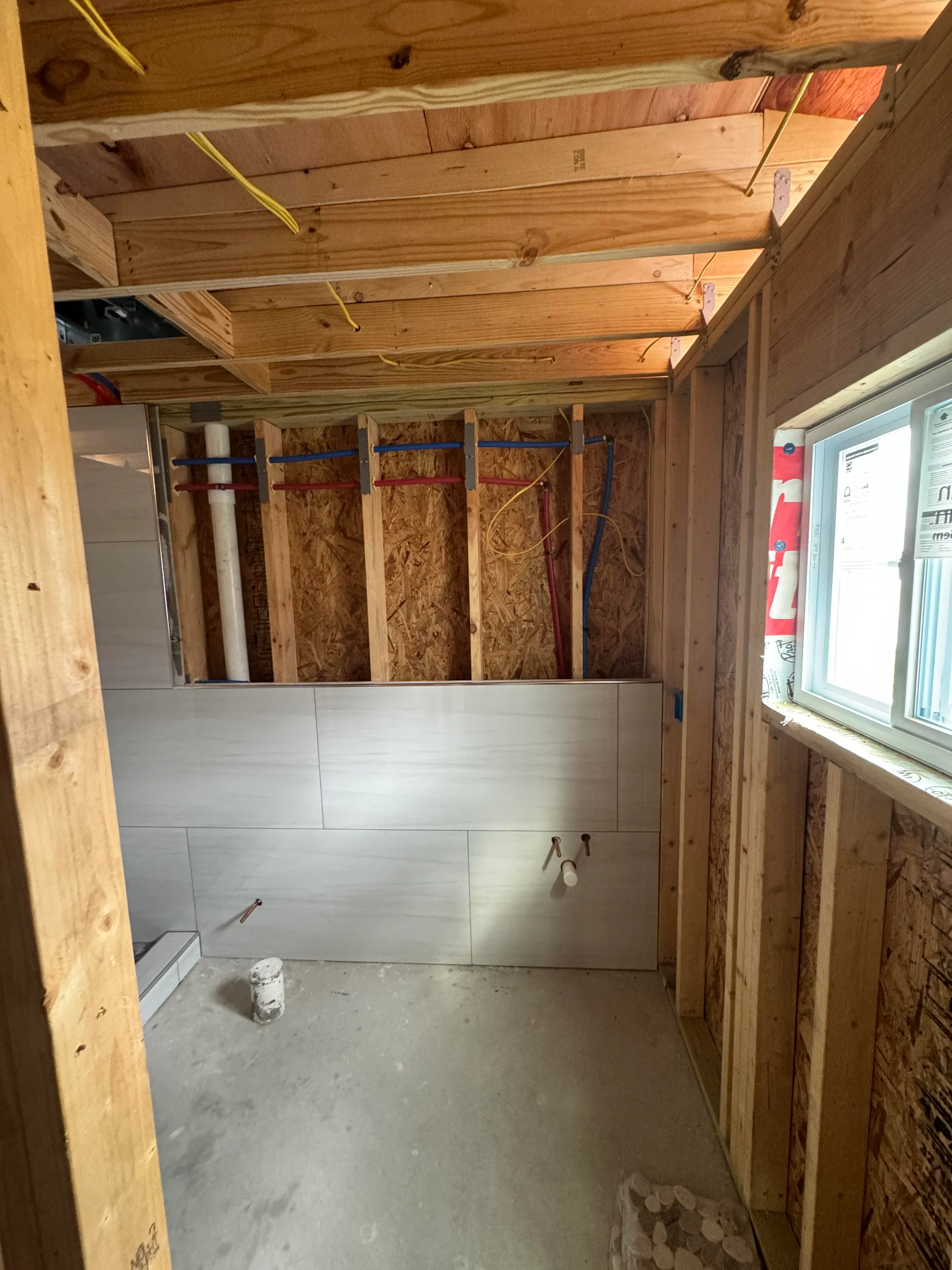 Bathroom interior framing with wood studs, OSB sheathing, and drywall installation in progress
