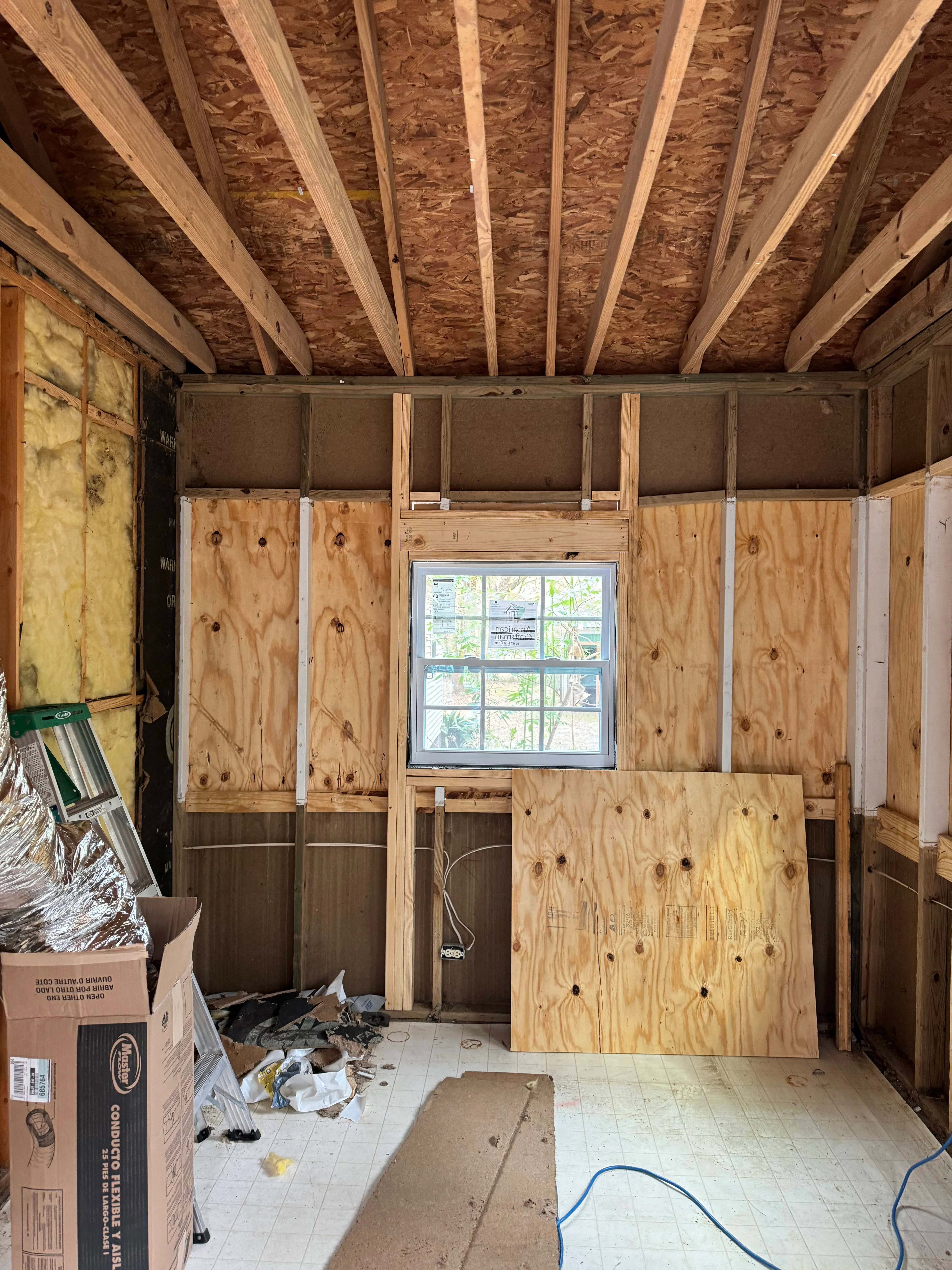 Interior framing with wooden studs, OSB sheathing, and installed window in New Orleans renovation