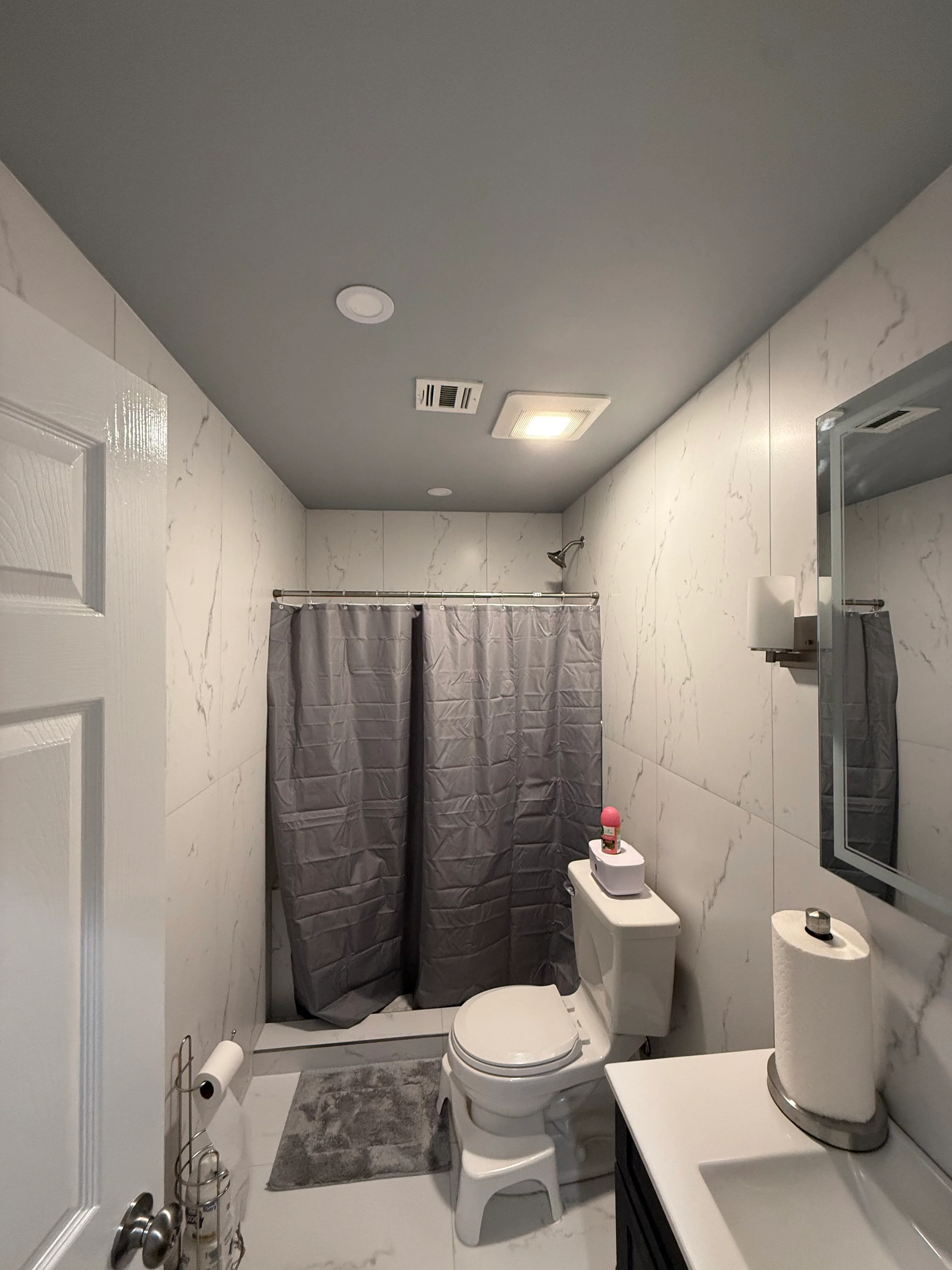 Modern bathroom with marble tile walls, gray shower curtain, white vanity, and recessed lighting