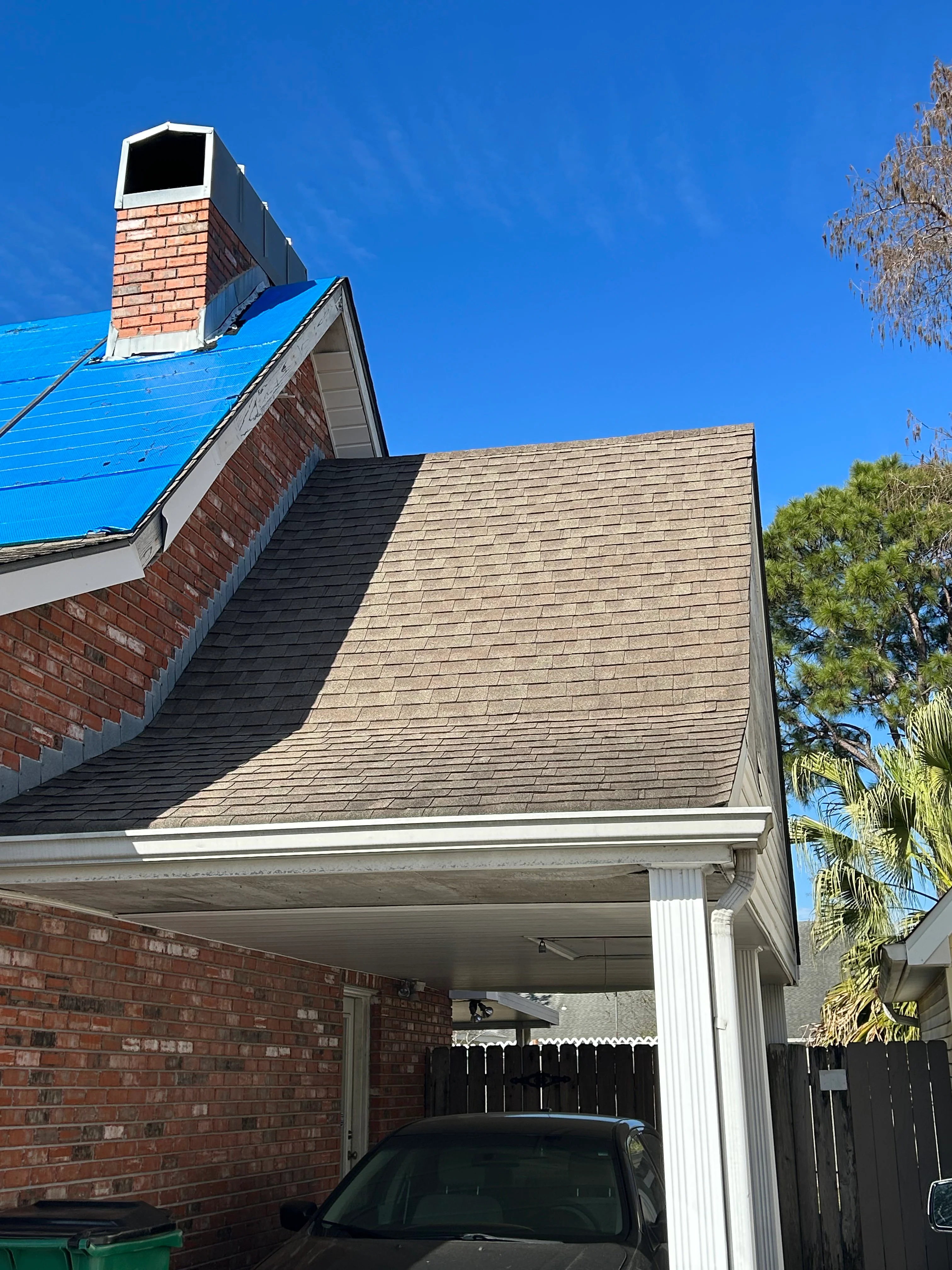 New tan shingle roof installed on brick home with white trim and carport