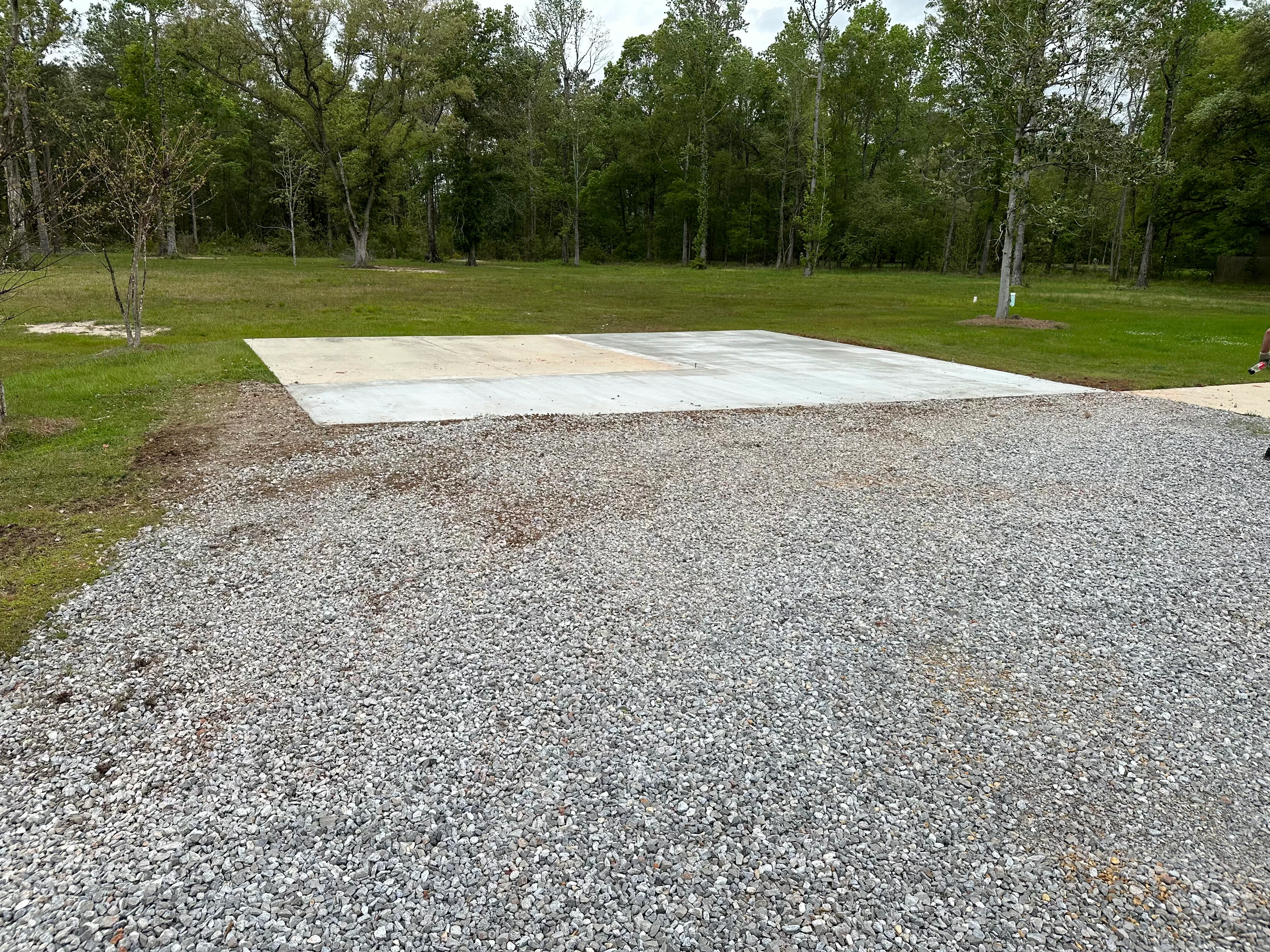Concrete foundation pad with gravel base on cleared lot surrounded by trees
