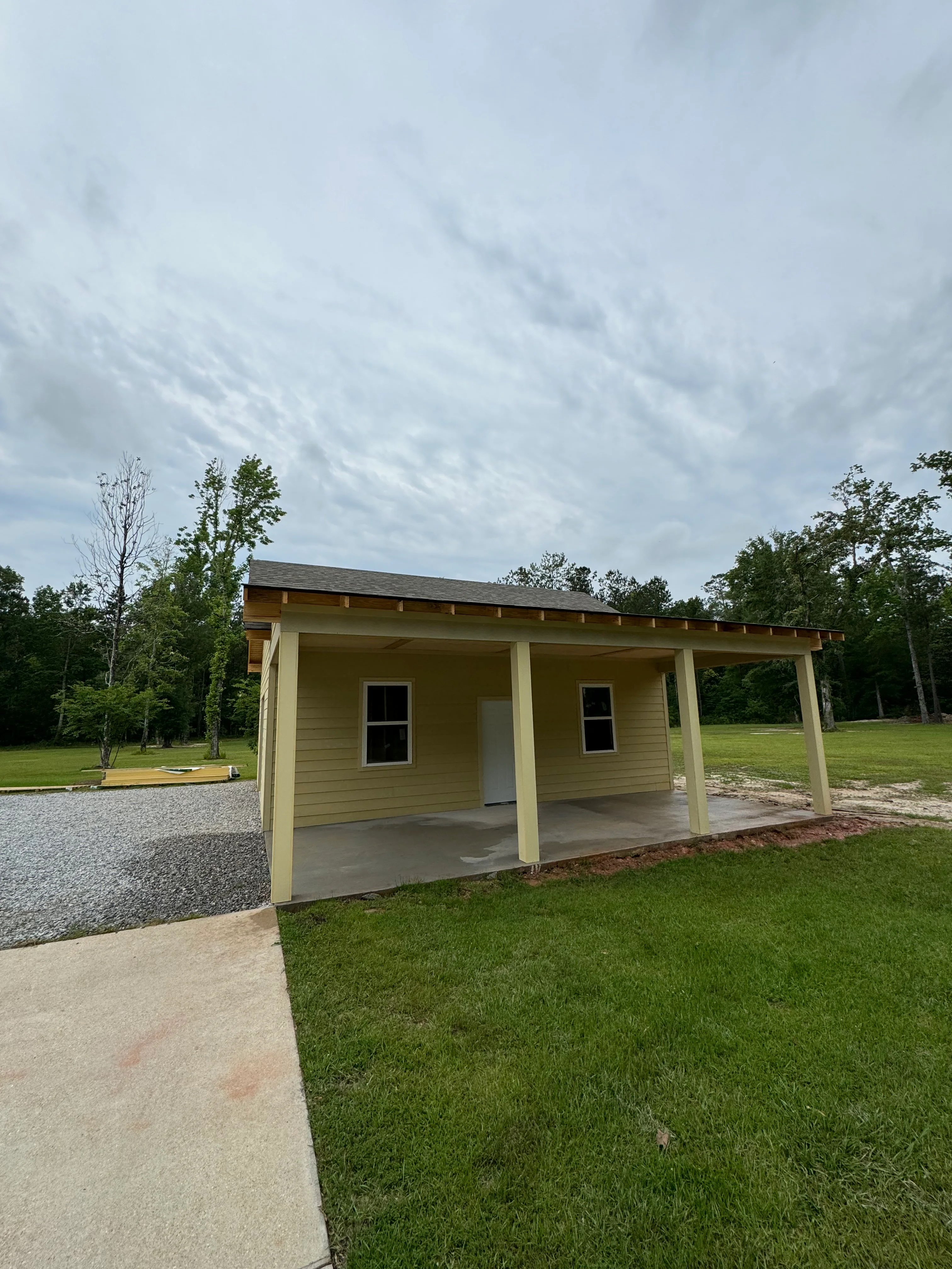 Newly constructed tan pavilion with covered porch, metal roof, and concrete foundation on grassy lot