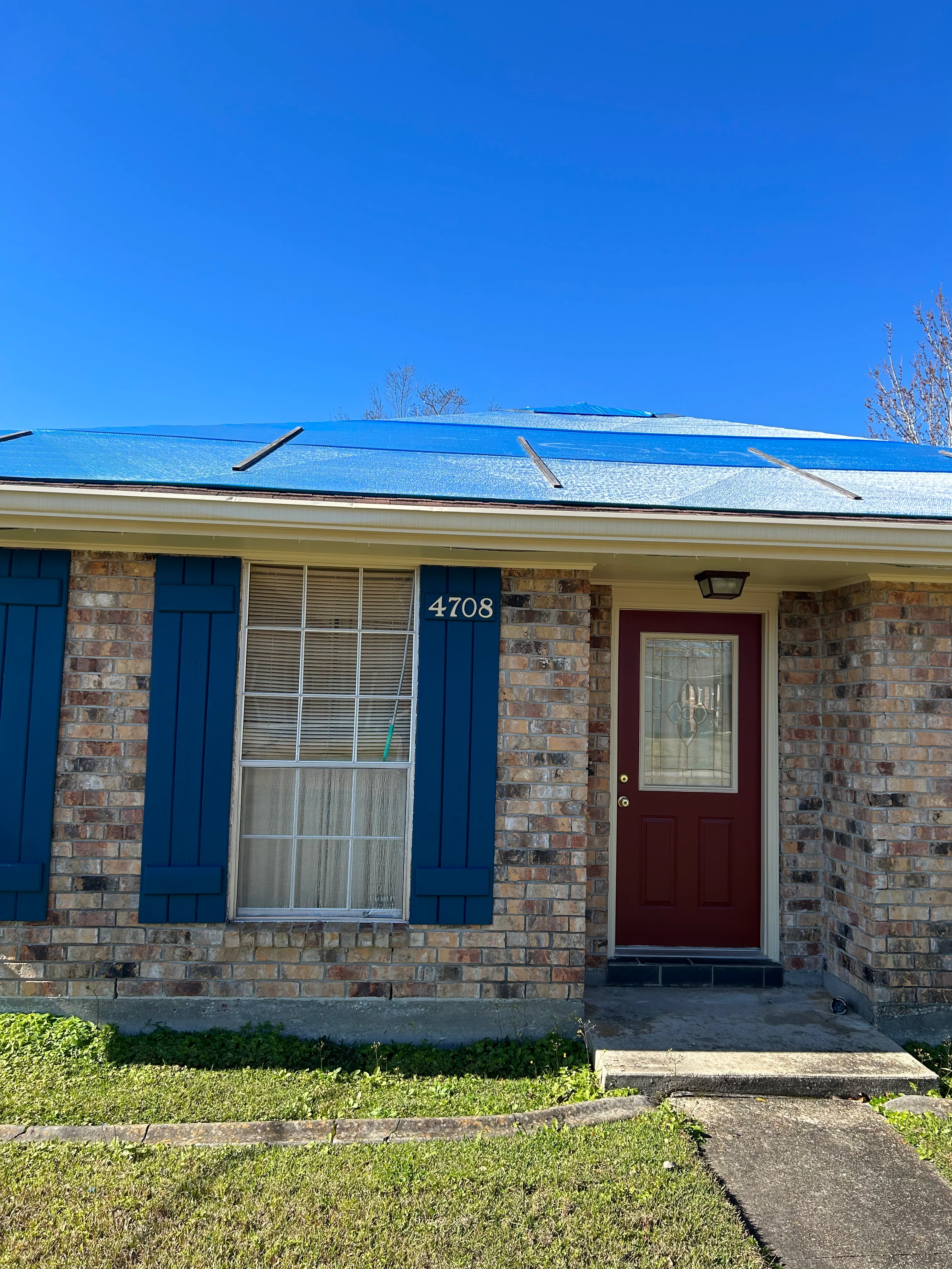 New blue shingle roof installed on brick residential home with red door and blue shutters