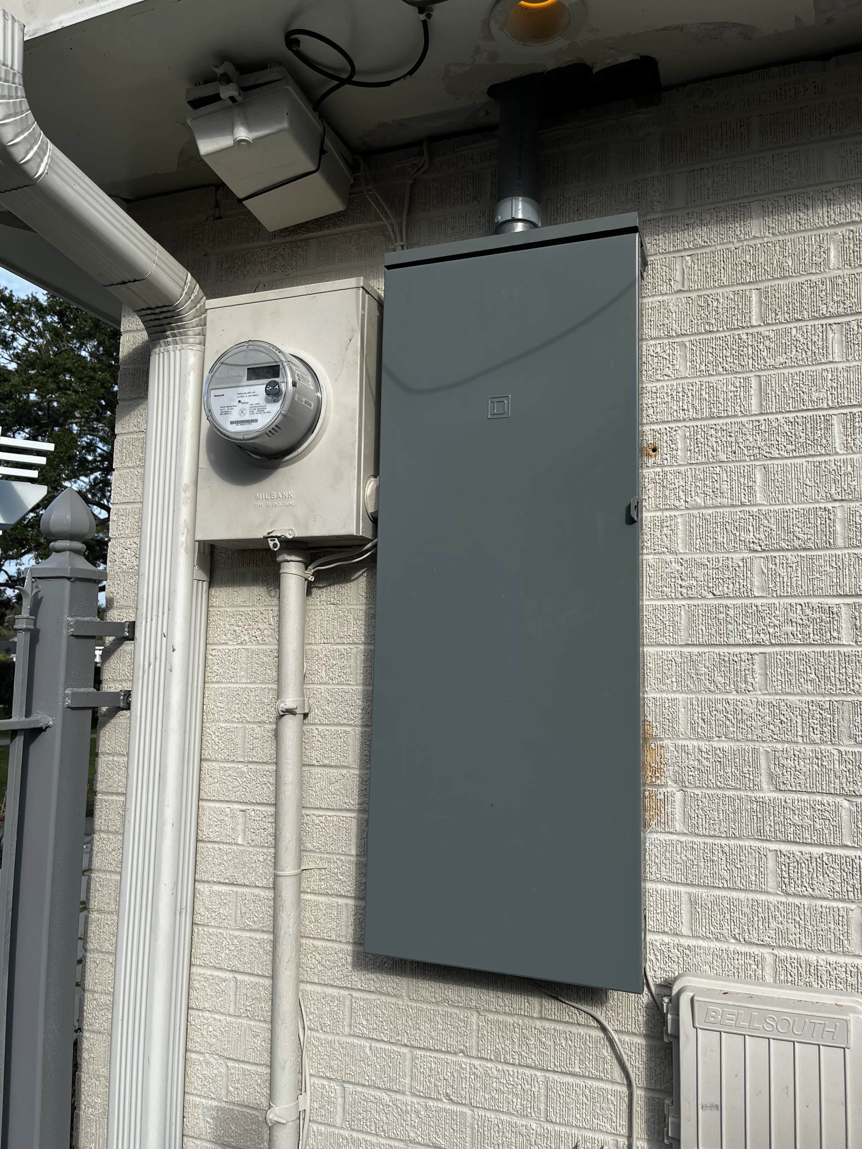 Electrical meter and gray service panel mounted on cream brick wall with conduit