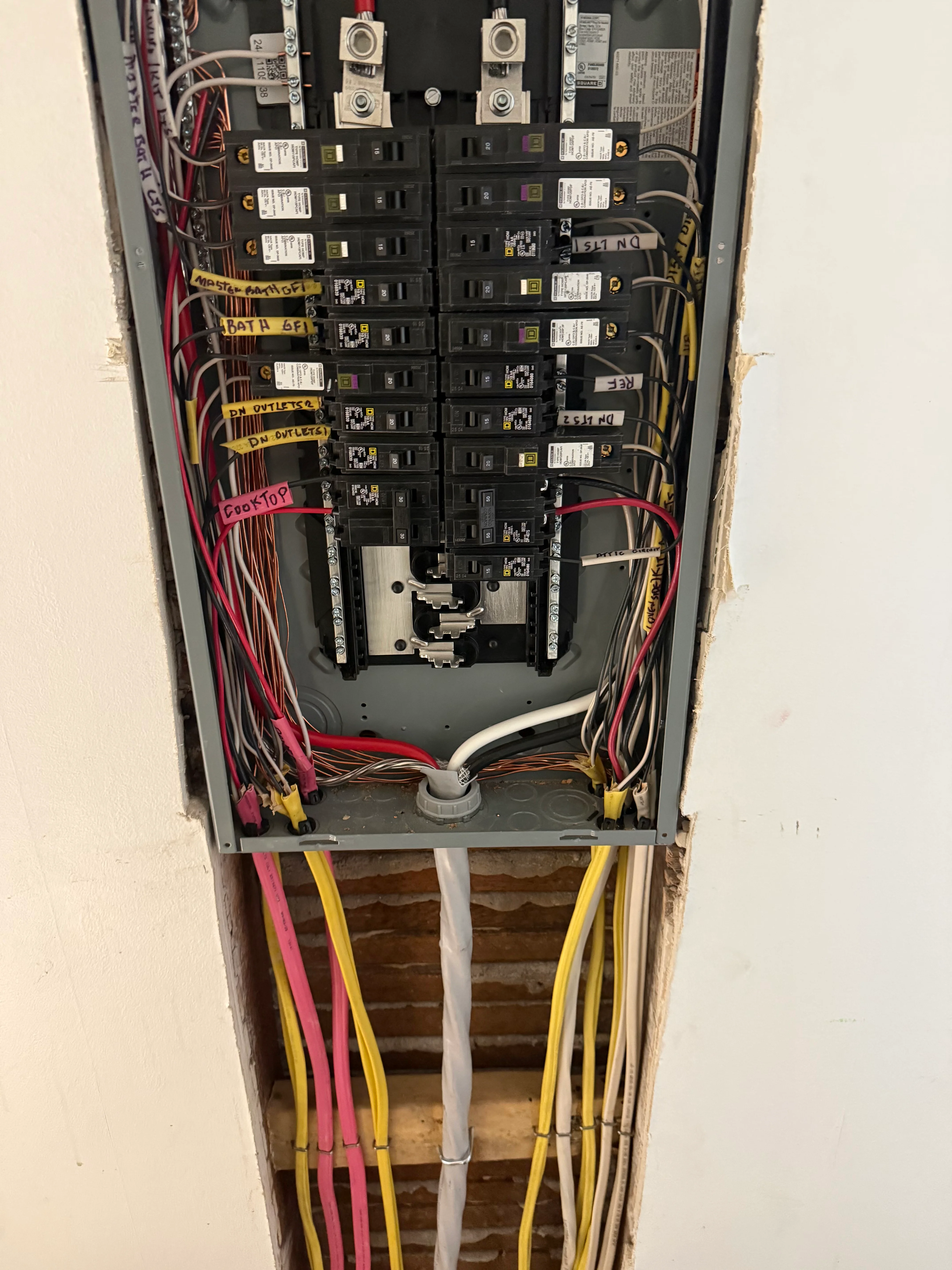 Electrical panel with dual breakers, color-coded wiring, and labeled circuits installed in wall cavity