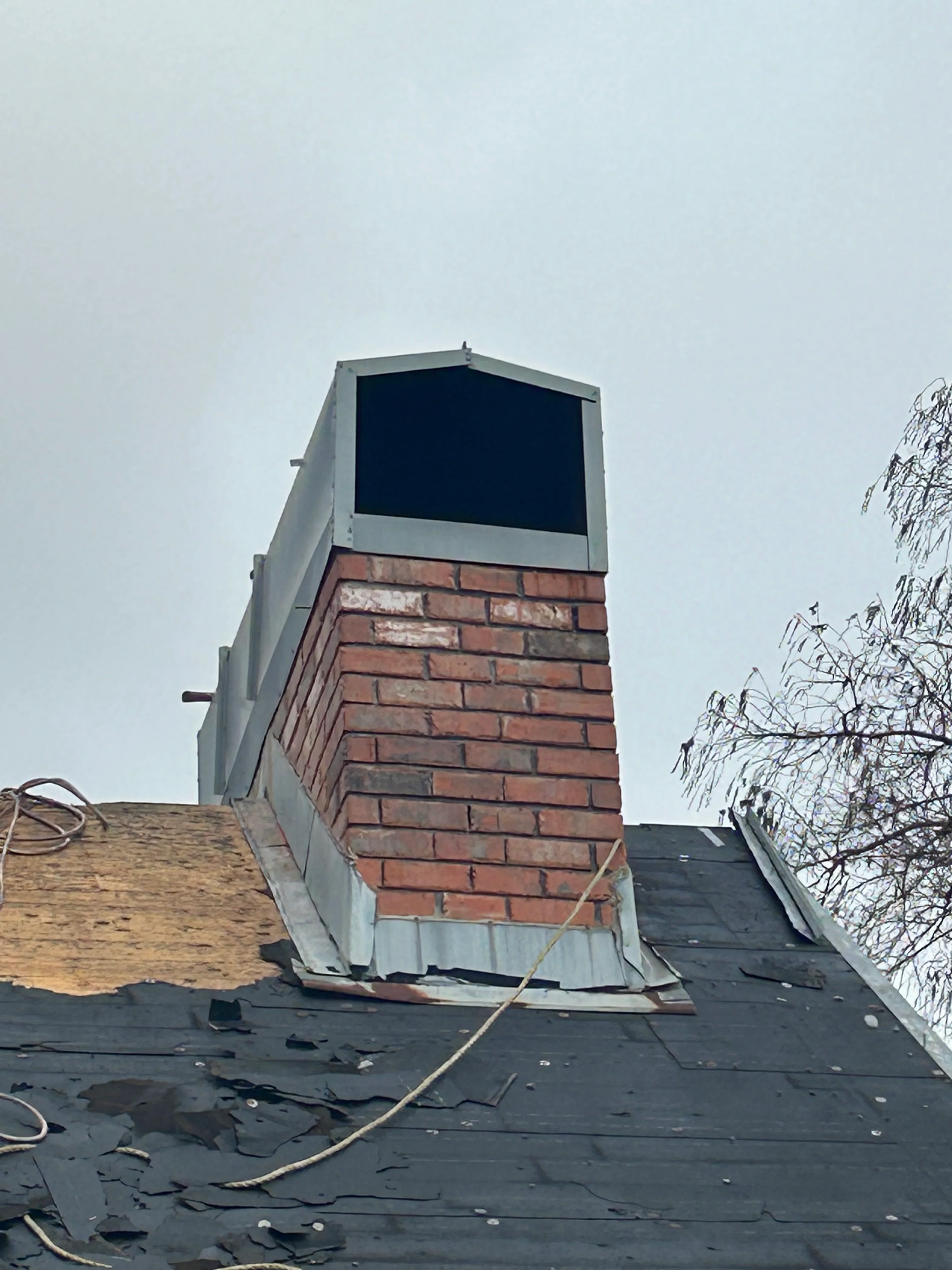Rebuilt brick chimney with metal cap on residential roof with black membrane